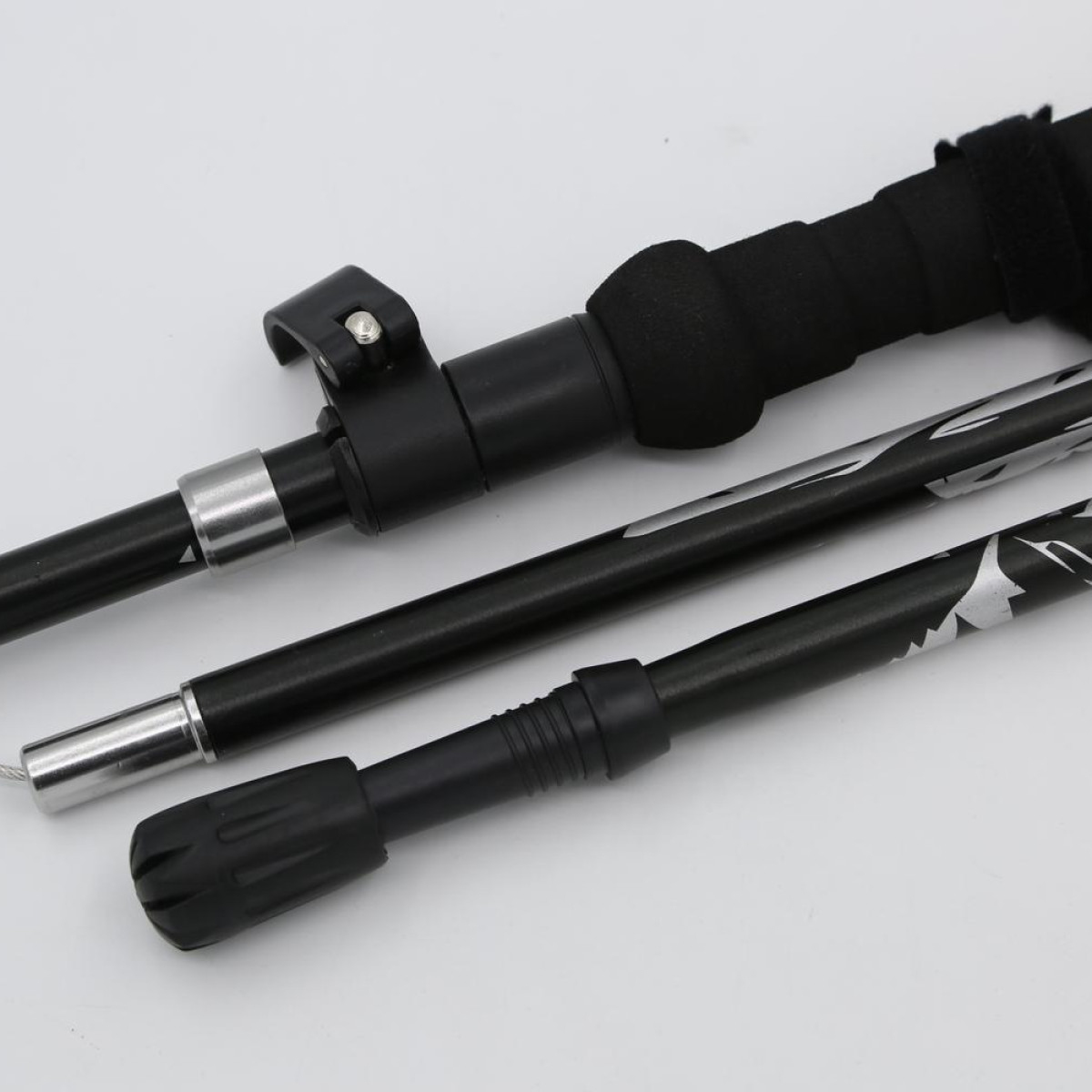 Zestaw kijków trekkingowych. Kije są czarne z szarą i srebrną grafiką. Tło jest białe.