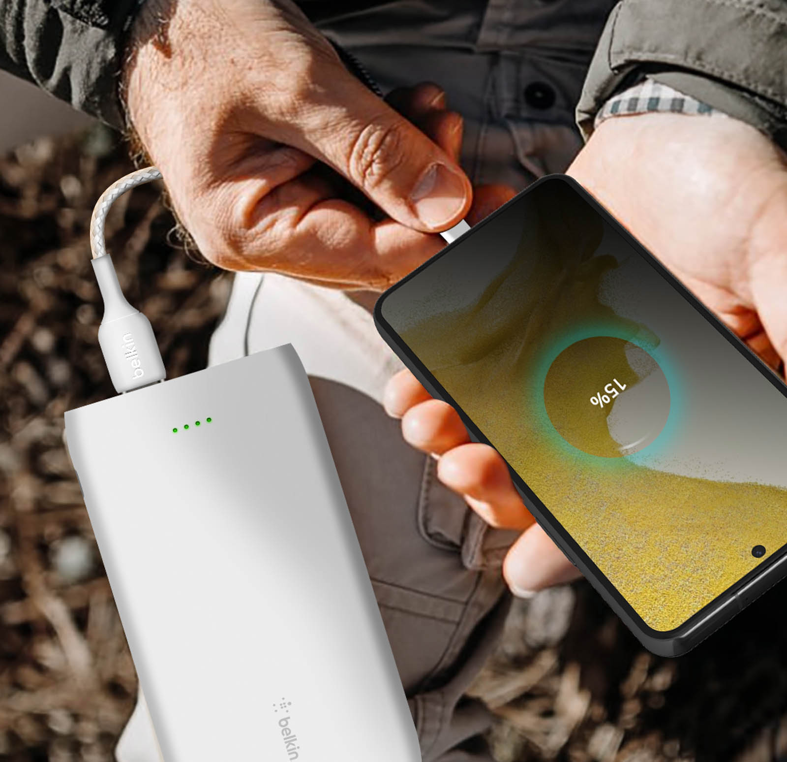 Handen laden een zwarte smartphone op met een witte powerbank. Scherm toont 15%.