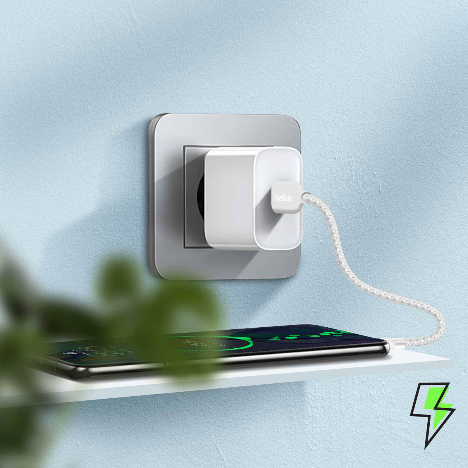 Witte Belkin lader aangesloten, laadt zwarte telefoon op, blauwe muur.