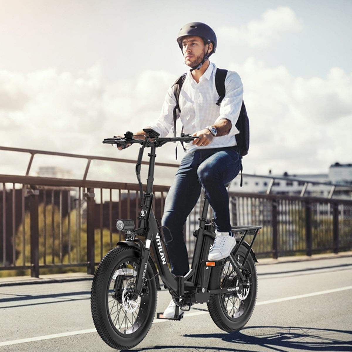 Mężczyzna jadący czarnym rowerem elektrycznym po drodze. Ma kask i plecak. Tłem jest most i niebo.