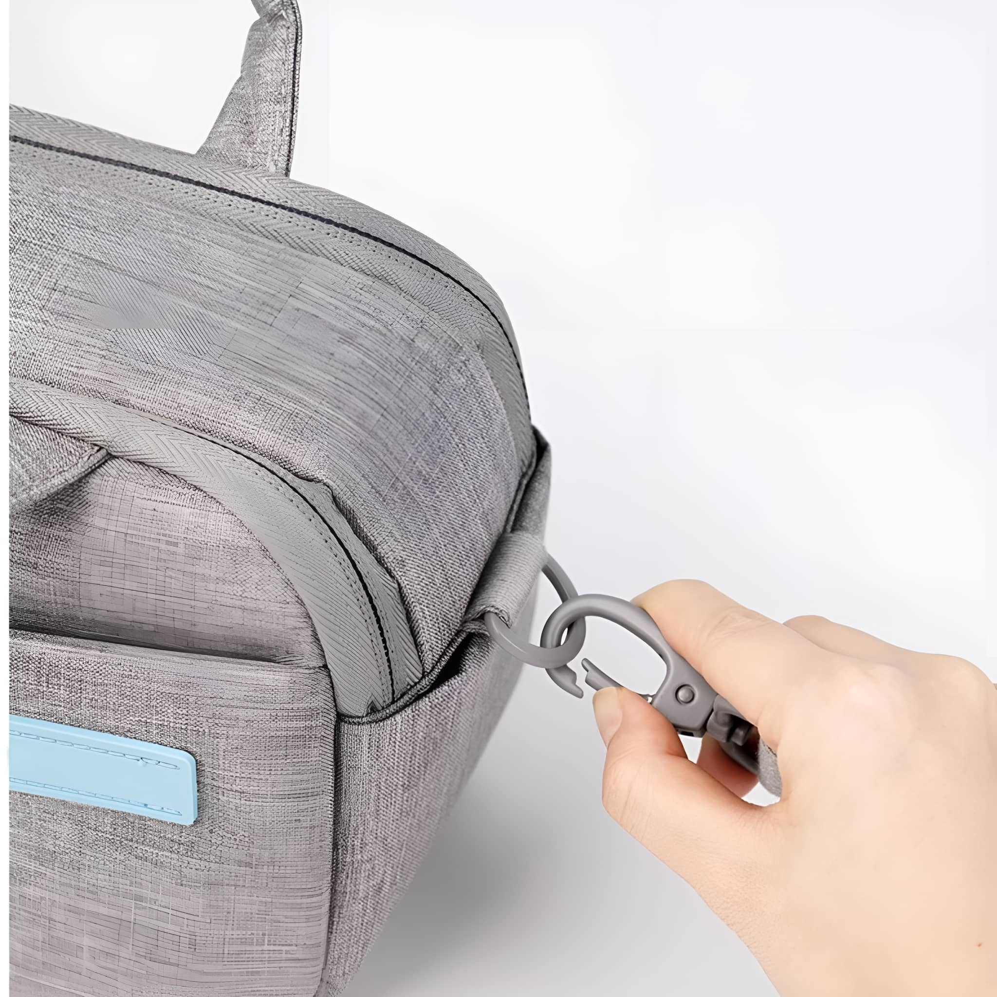 Eine Hand befestigt einen Beutelriemen. Die Tasche ist grau. Der Hintergrund ist weiß.