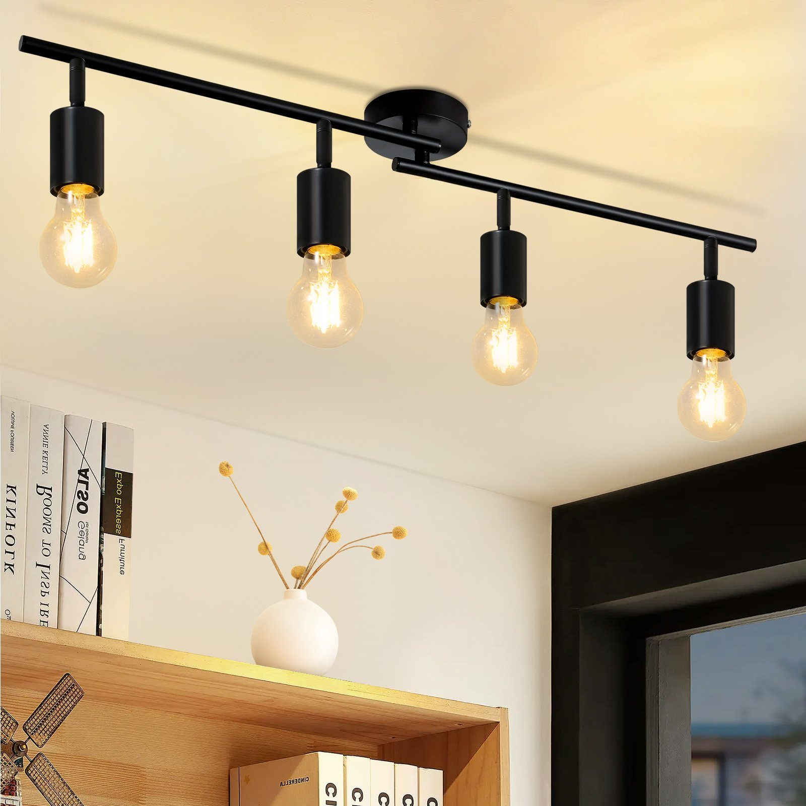 Cztery czarne reflektory na czarnym drążku. Drążek jest zamontowany na białym suficie. Widoczny biały wazon i książki.