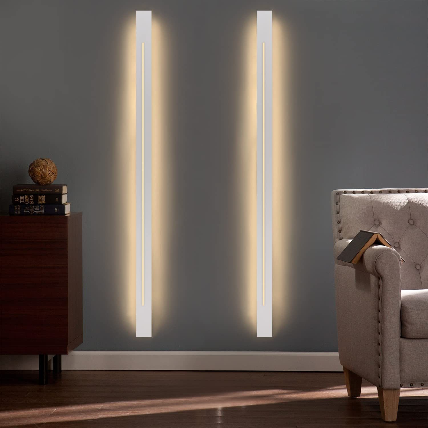 Due lunghe applique bianche con una linea di luce, montate su un muro grigio scuro. Sedia visibile.