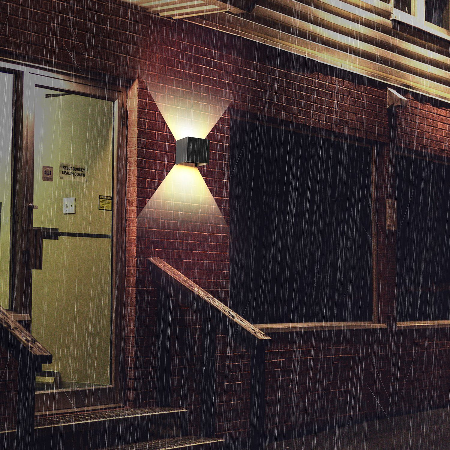 Zewnętrze budynku w deszczu. Światła świecą z oprawy naściennej.