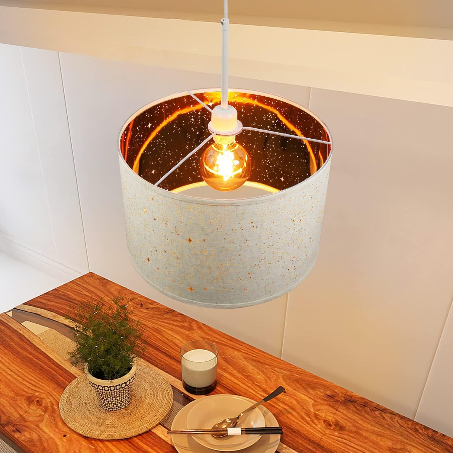 Lampa wisząca nad drewnianym stołem. Lampa ma okrągły klosz z gwiazdami i żarówkę.