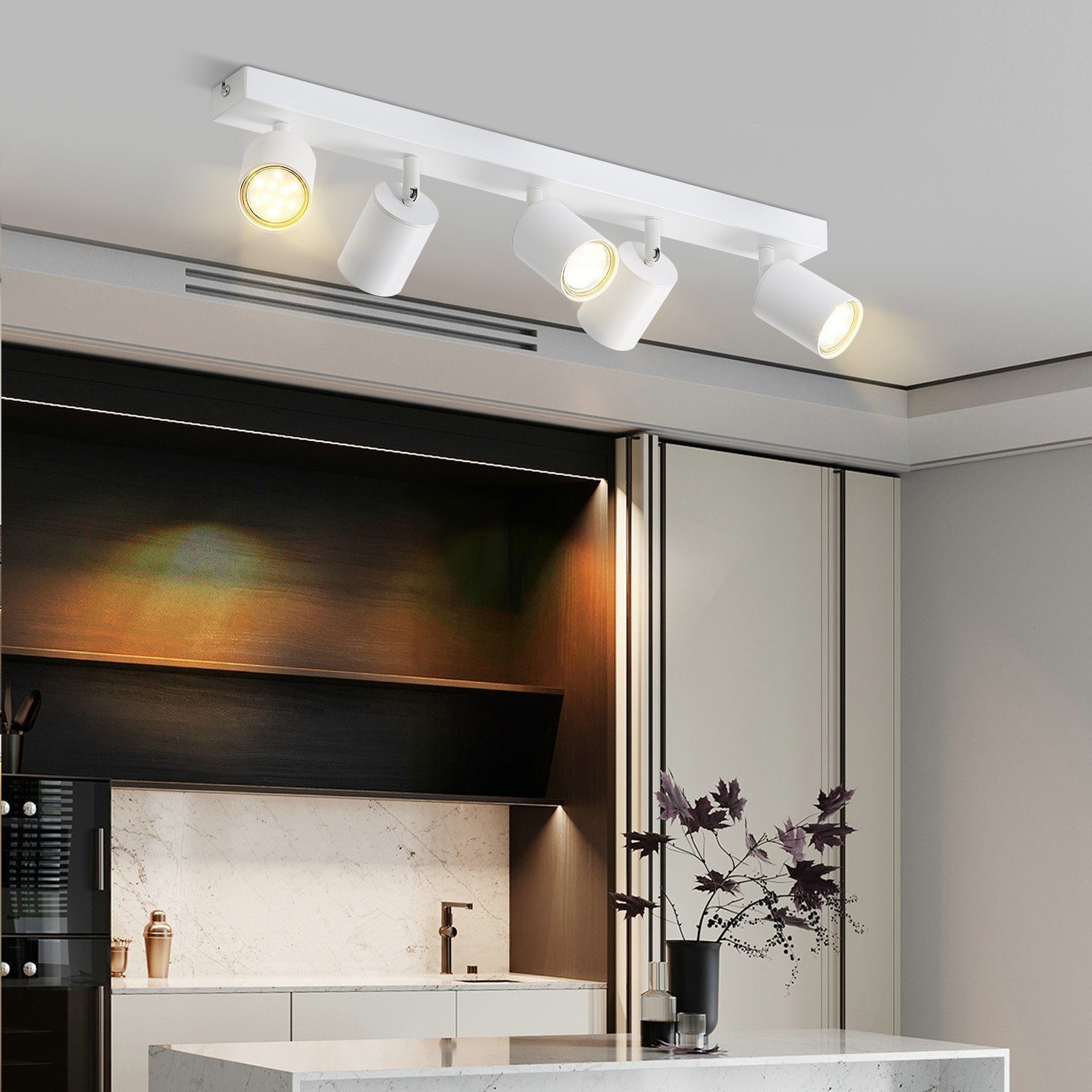 Białe reflektory sufitowe. Kuchnia w tle z marmurowym blatem i roślinami.