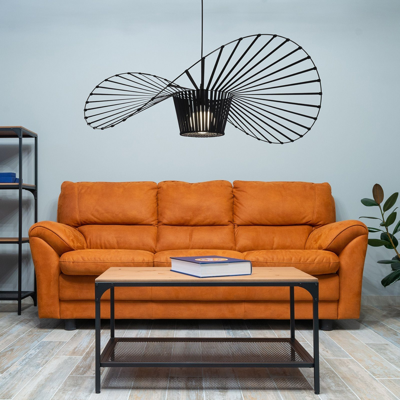 Orangefarbenes Sofa, Holztisch und schwarze Deckenlampe. Auf dem Tisch liegt ein Buch. Weiße Wand.