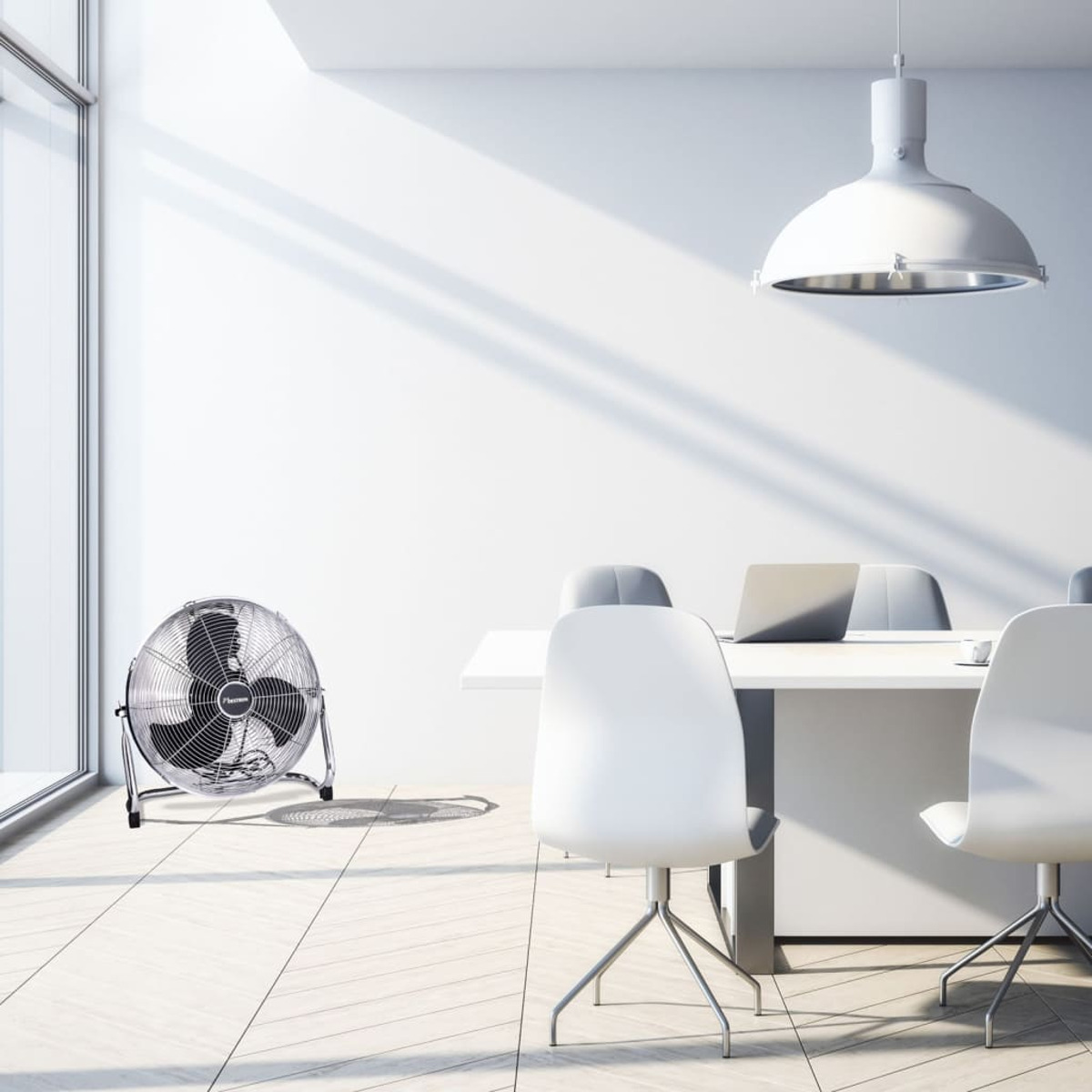 Un grande ventilatore argentato in una stanza bianca. Un tavolo e sedie bianche sullo sfondo.