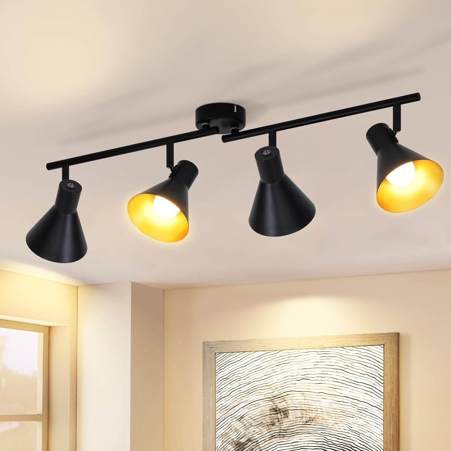 Czarna lampa sufitowa z czterema regulowanymi, czarnymi reflektorami. Tło to beżowa ściana.