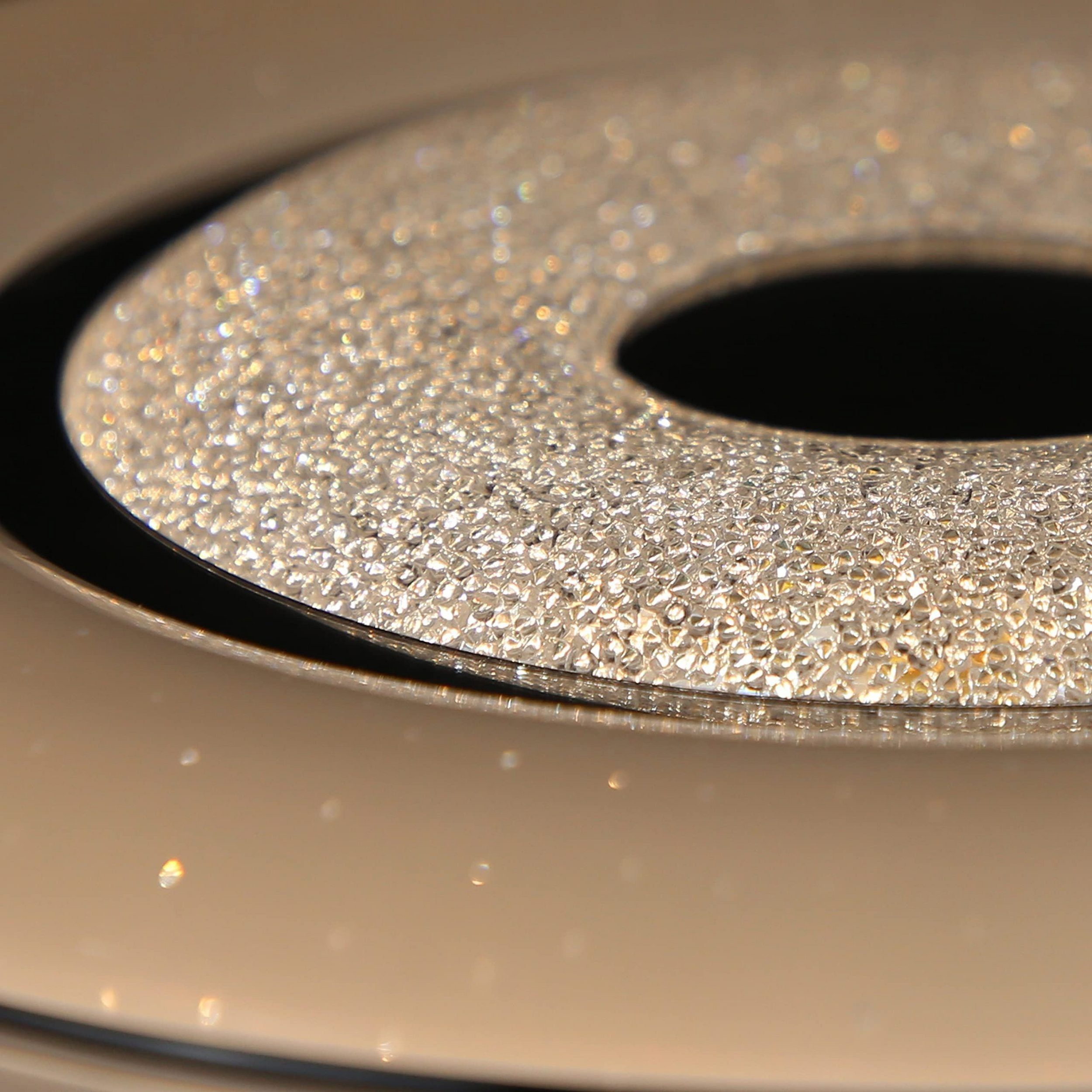 Zbliżenie na nowoczesną, pokrytą kryształami, okrągłą oprawę oświetleniową. Odbijająca powierzchnia poniżej.