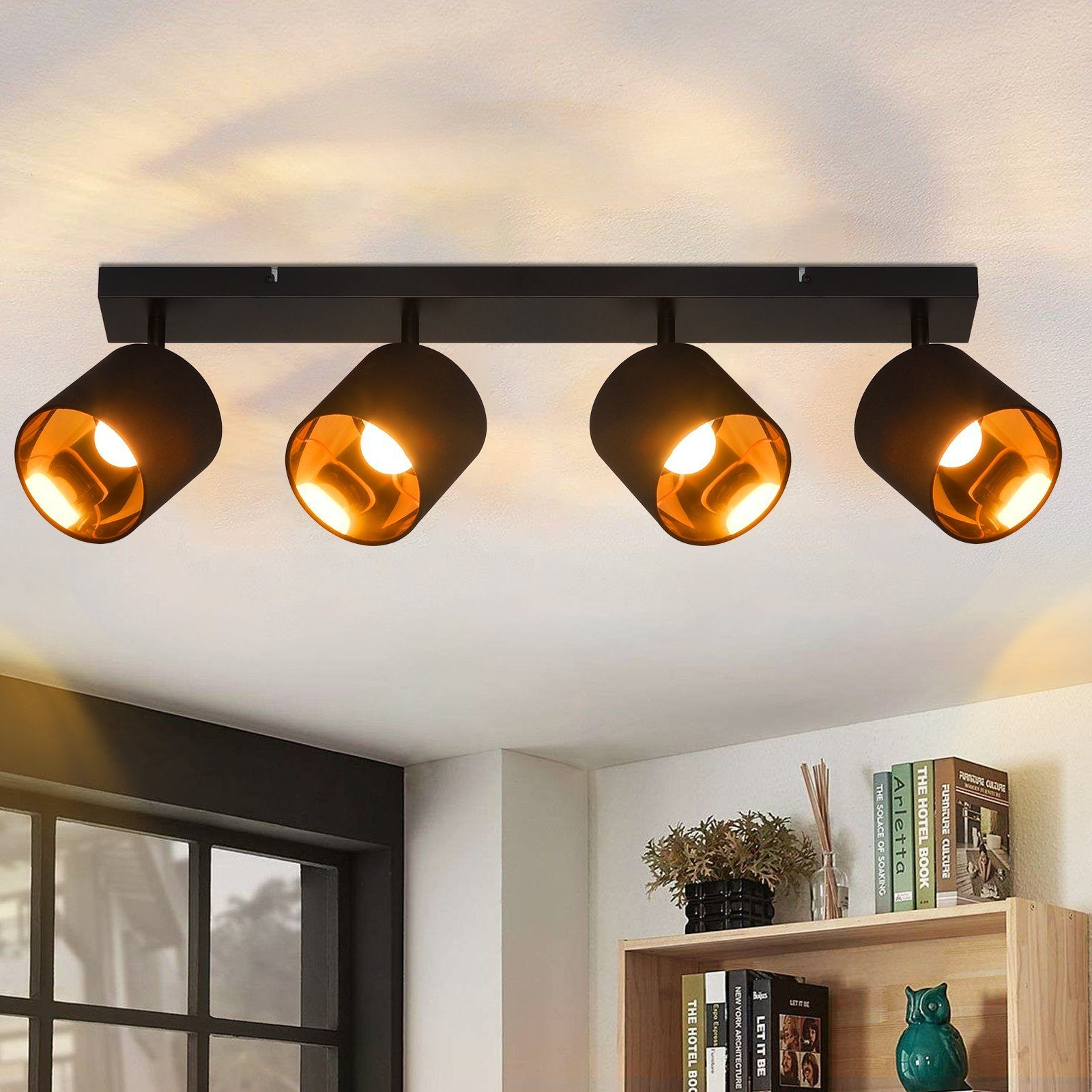 Un'apparecchio per binario nero con quattro faretti orientati verso il basso, con un soffitto bianco e una mensola in legno.
