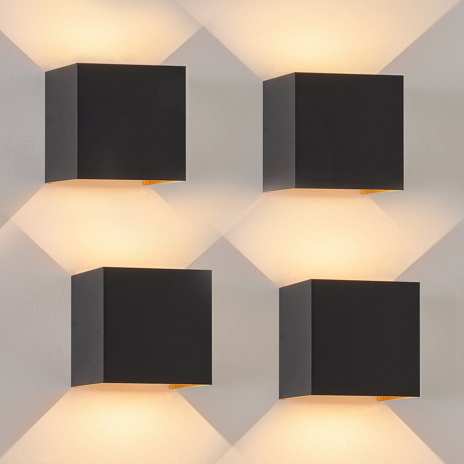 Cztery czarne kwadratowe lampy ścienne ze złotymi wnętrzami zamontowane na białej ścianie.
