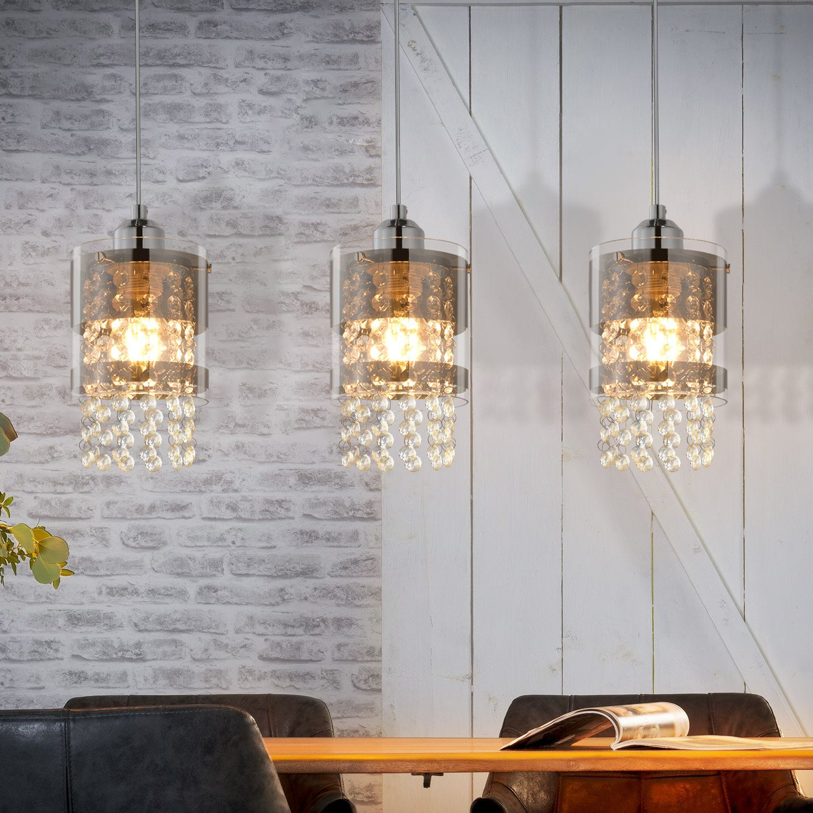 Trzy kryształowe lampy wiszące zwisają nad drewnianym stołem na tle ceglanej ściany.