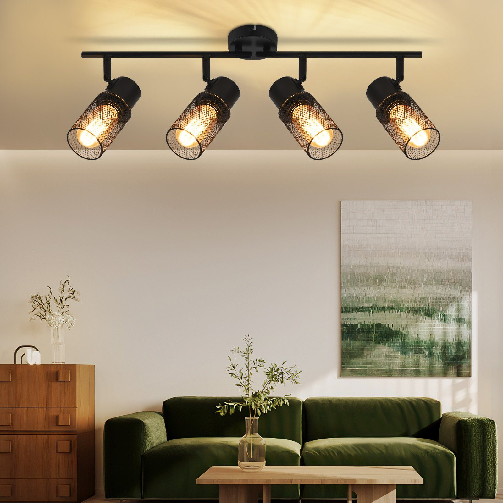 Illuminazione a binario nera con quattro faretti sul soffitto, che illuminano un divano verde e un tavolo di legno.