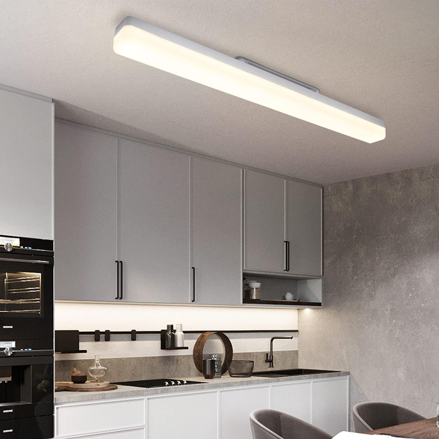 Długa, biała, prostokątna lampa sufitowa LED nad szafkami kuchennymi i zlewem.