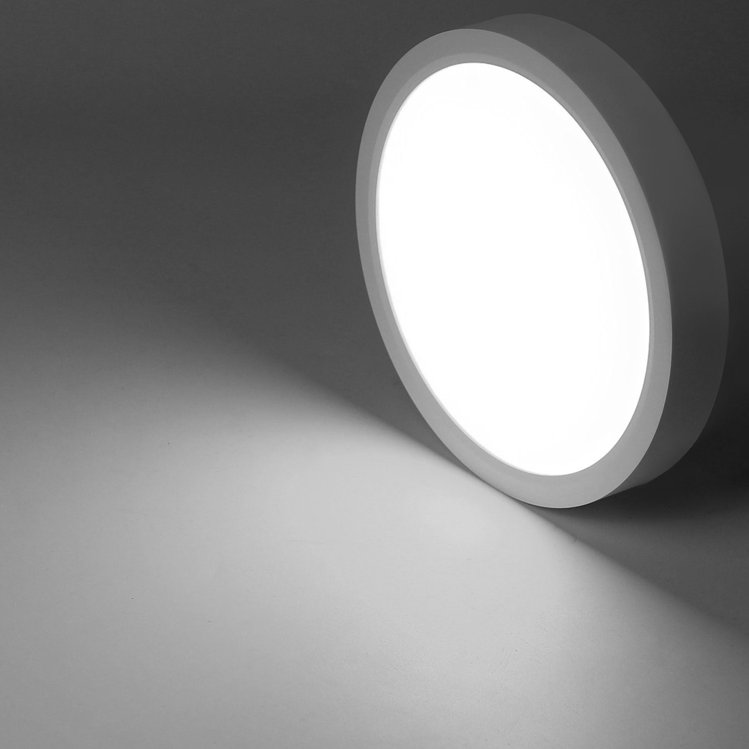 Okrągła, biała lampa sufitowa z jasnym blaskiem, rzucająca cień na powierzchnię.