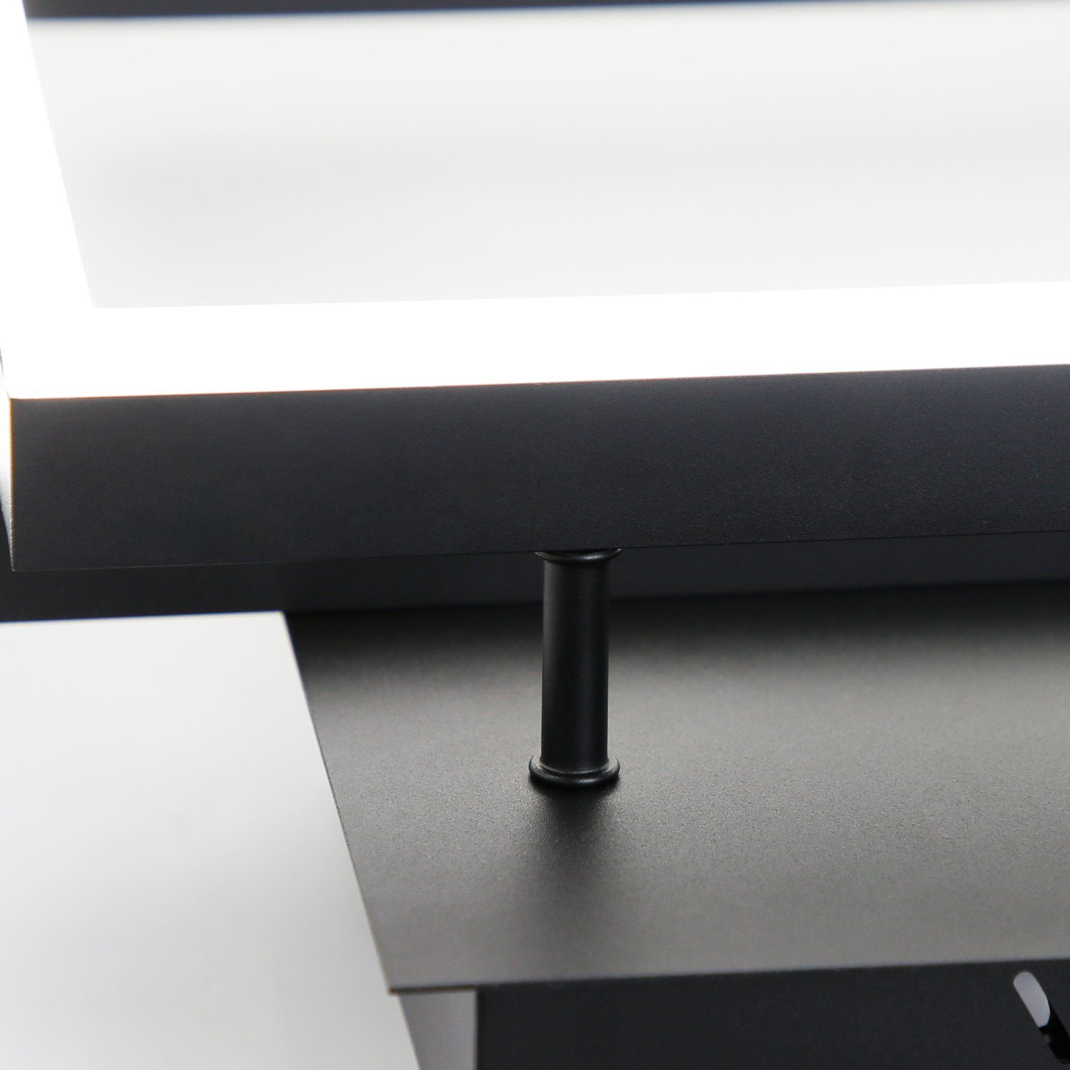 Zbliżenie czarnej oprawy oświetleniowej. Białe światło świeci z prostokątnego otworu.