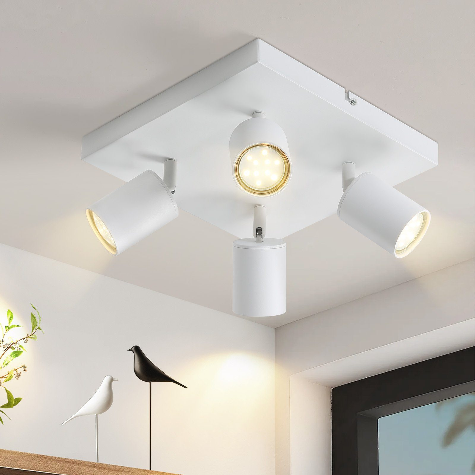 Una plafoniera bianca con tre faretti orientabili. Due piccole sculture di uccelli sono su una mensola sotto la luce.