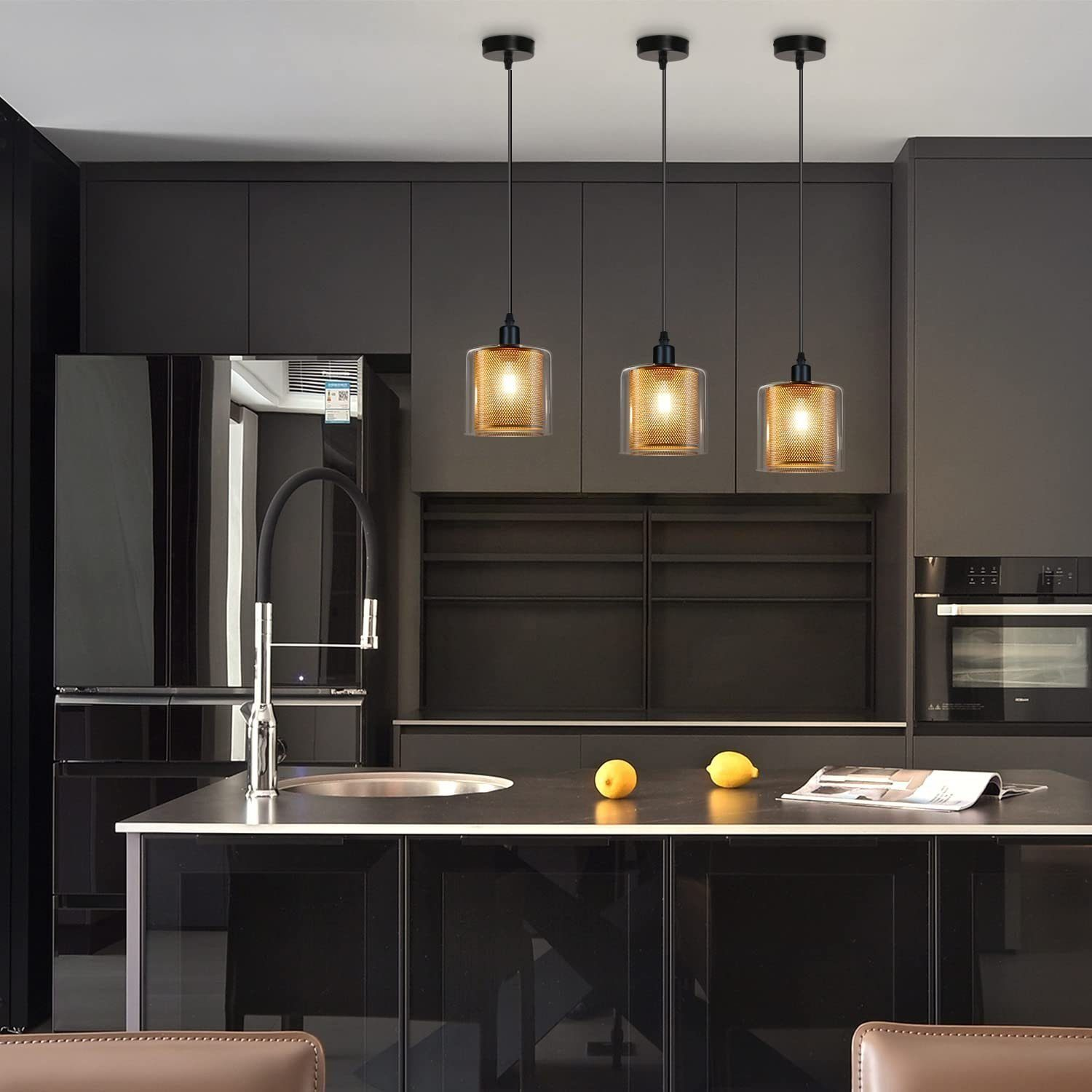 Trzy lampy wiszące z złotymi, siatkowymi kloszami wiszą w nowoczesnej czarnej kuchni z cytrynami.