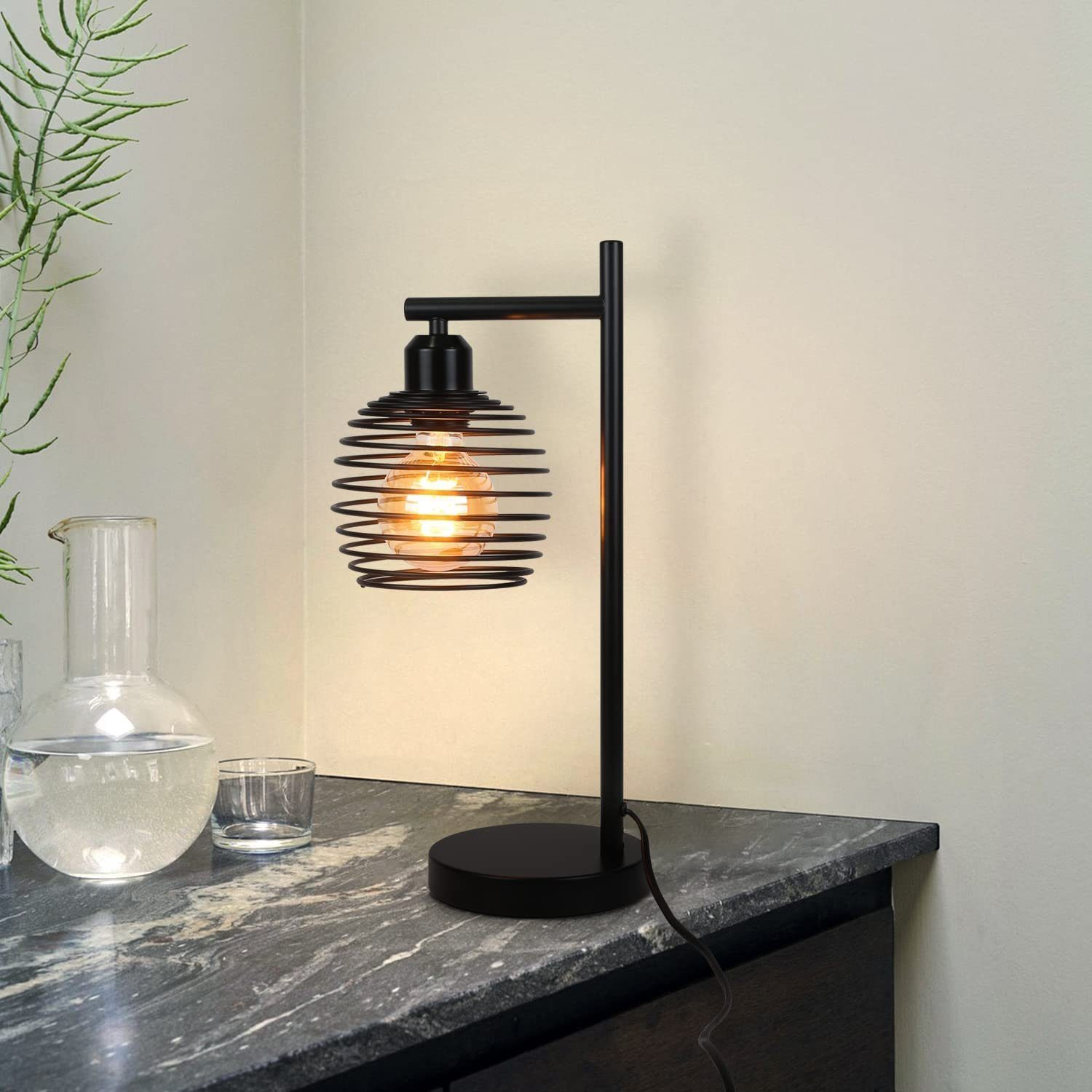 Czarna lampa w klatce spiralnej na stole. Szklana kolba i szklanka w tle, na ciemnej powierzchni.