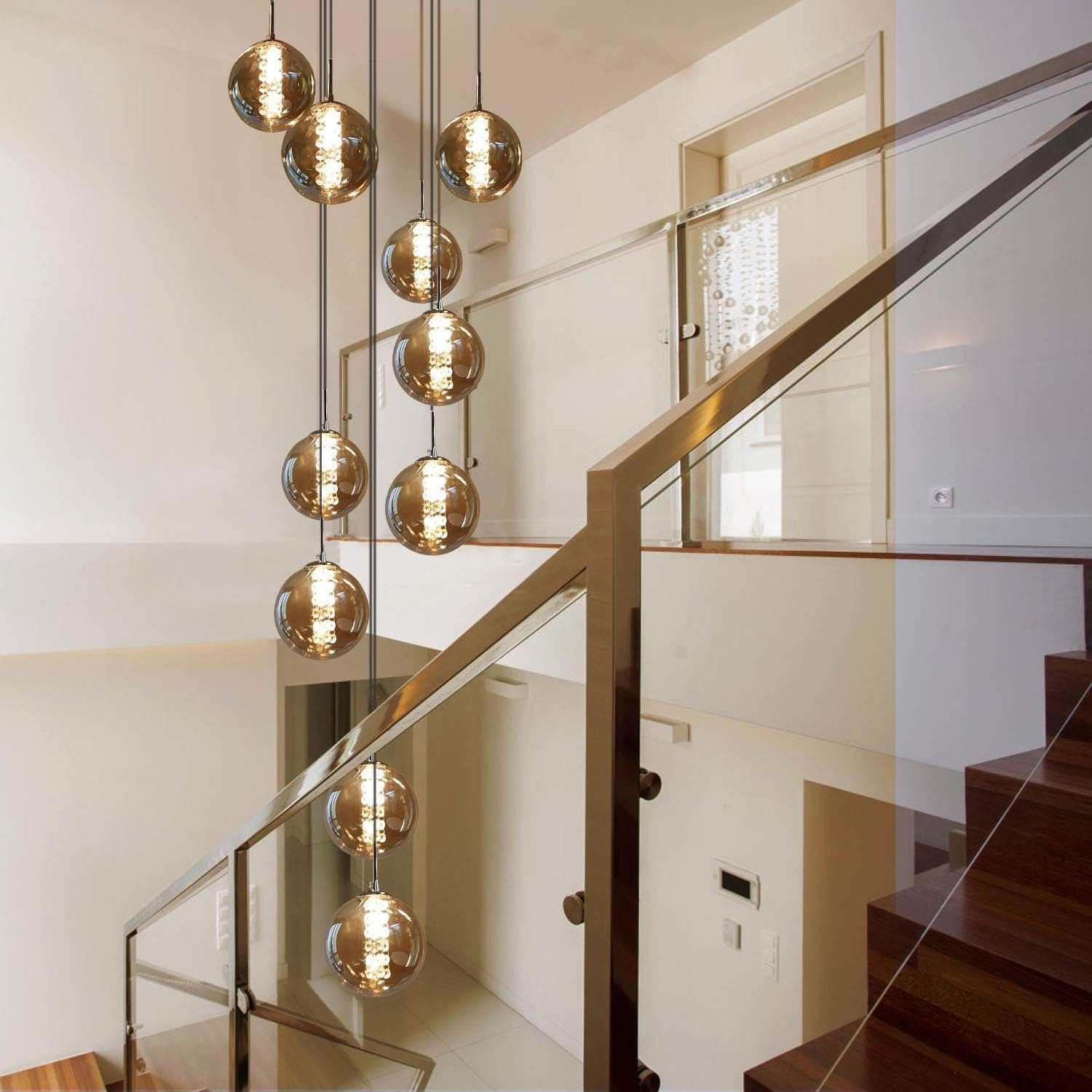 Schody ze szklanymi balustradami. Z sufitu zwisa seria kulistych świateł o ciepłym odcieniu.