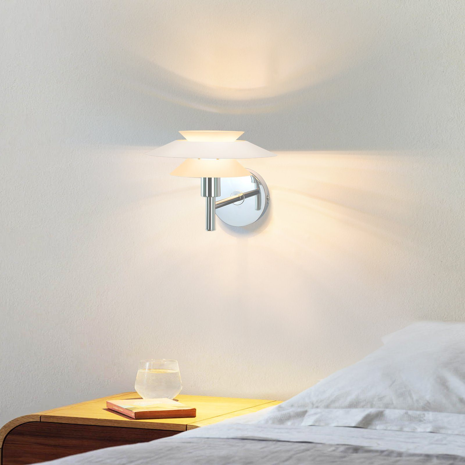 Lampa ścienna z trzema białymi abażurami nad stolikiem nocnym ze szklanką wody.