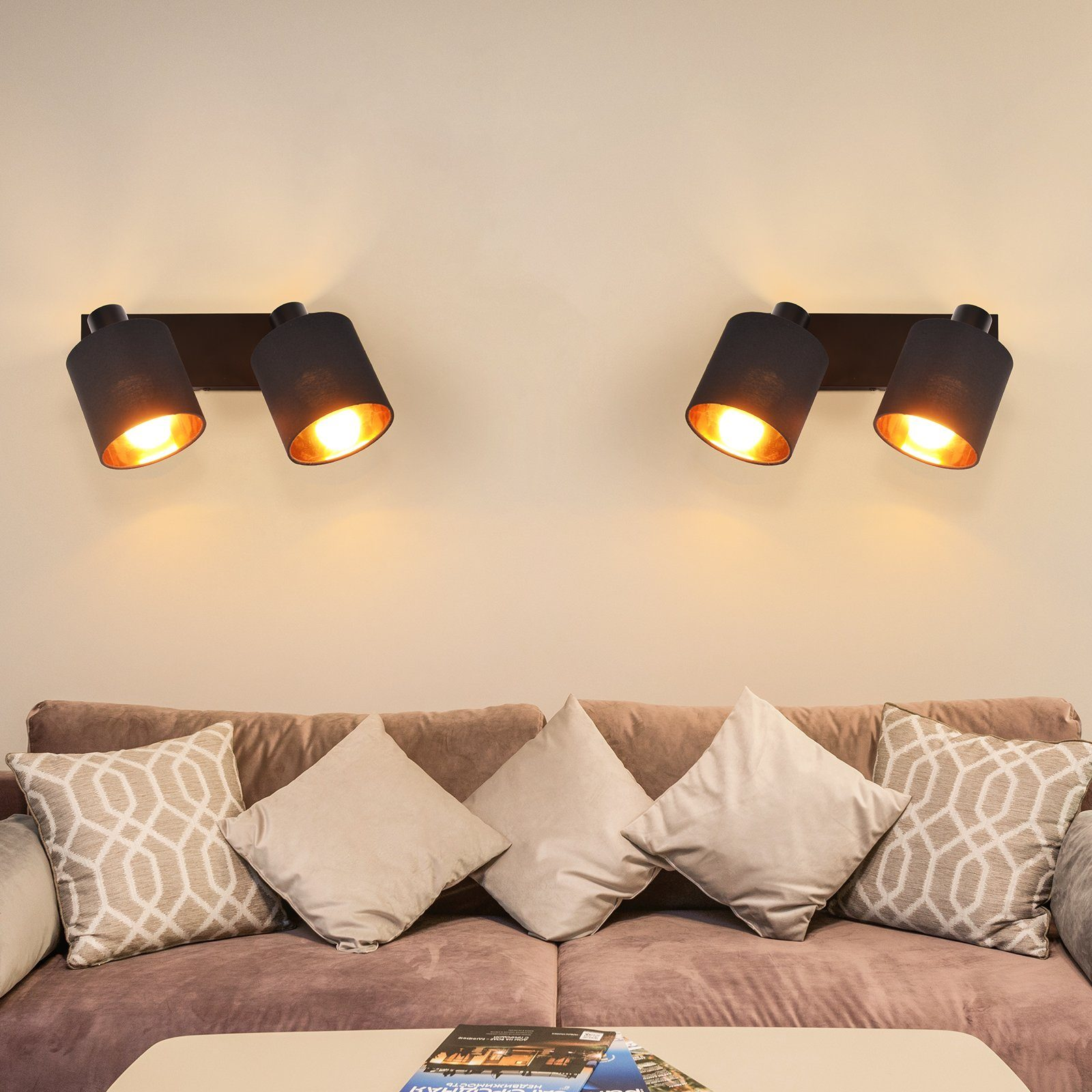 Dwie lampy ścienne z czarnymi kloszami i złotymi wnętrzami, oświetlające brązową sofę z beżowymi poduszkami.