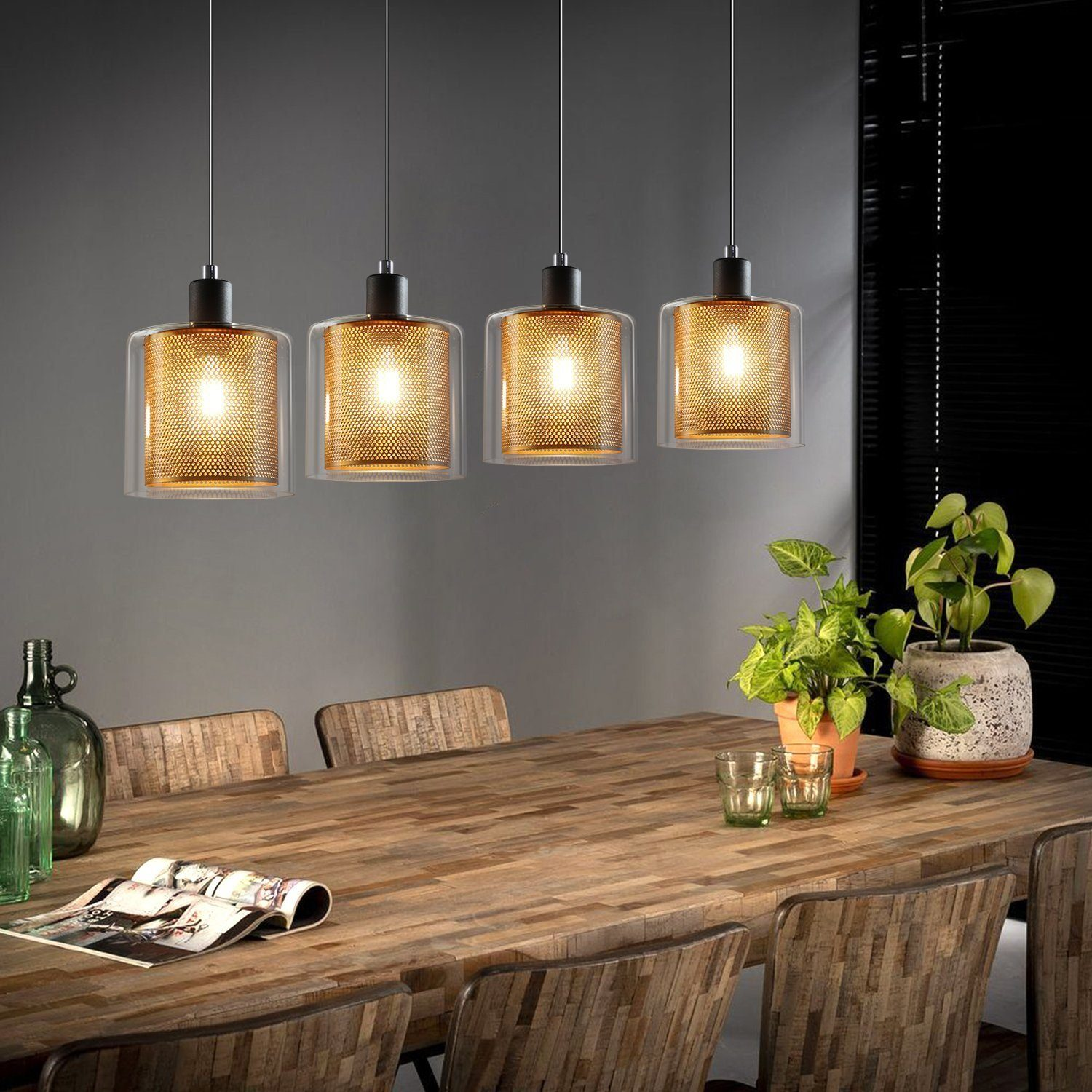 Cztery lampy wiszące nad drewnianym stołem z zieloną rośliną, butelką i szklankami.