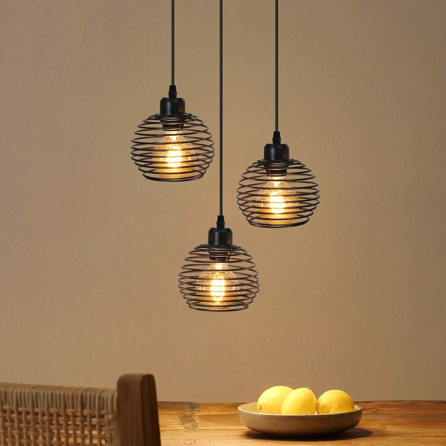 Trzy wiszące lampy z drucianą klatką wiszą nad powierzchnią, z jasną ścianą w tle.