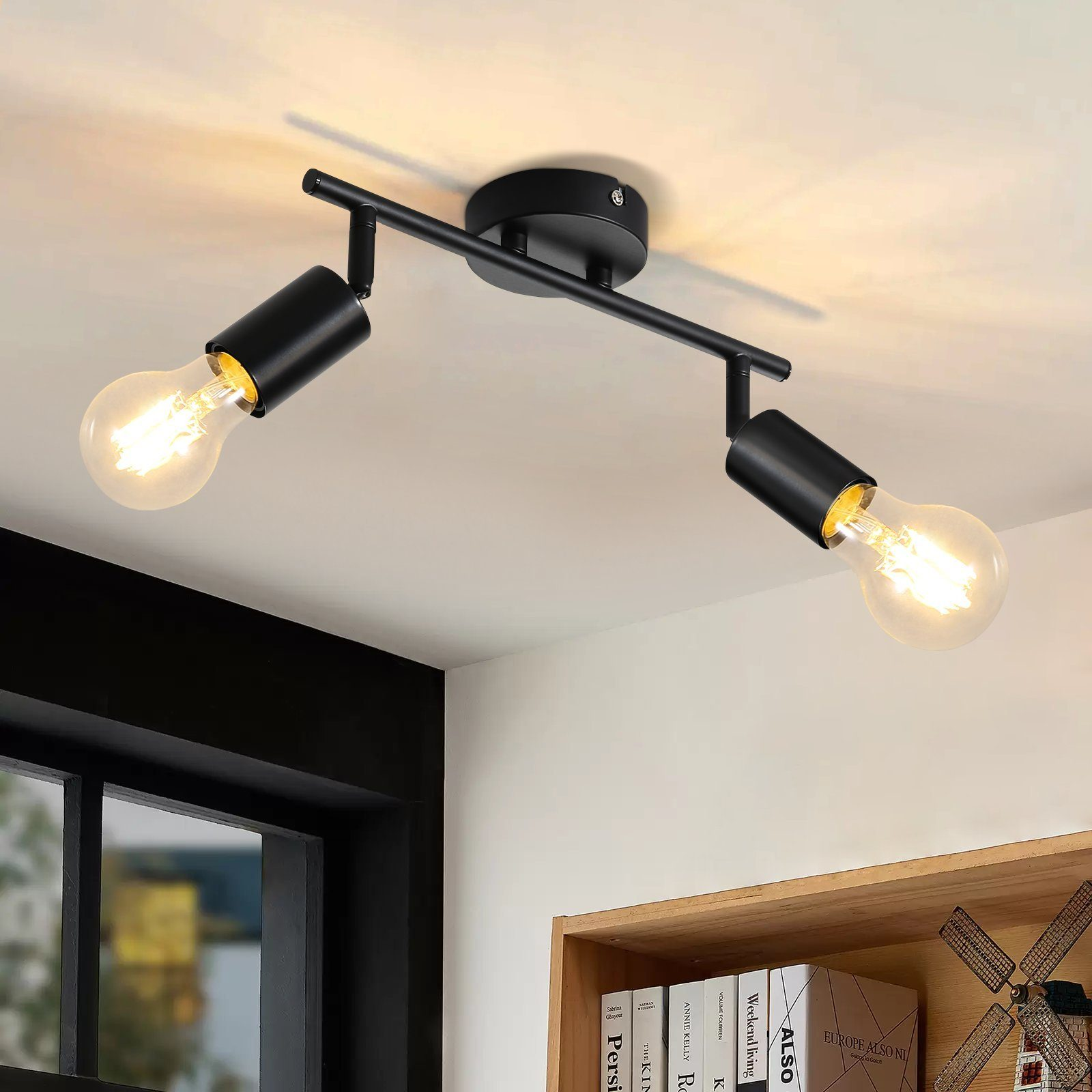 Czarna lampa sufitowa z dwiema żarówkami, oświetlająca pokój z drewnianą półką i książkami.