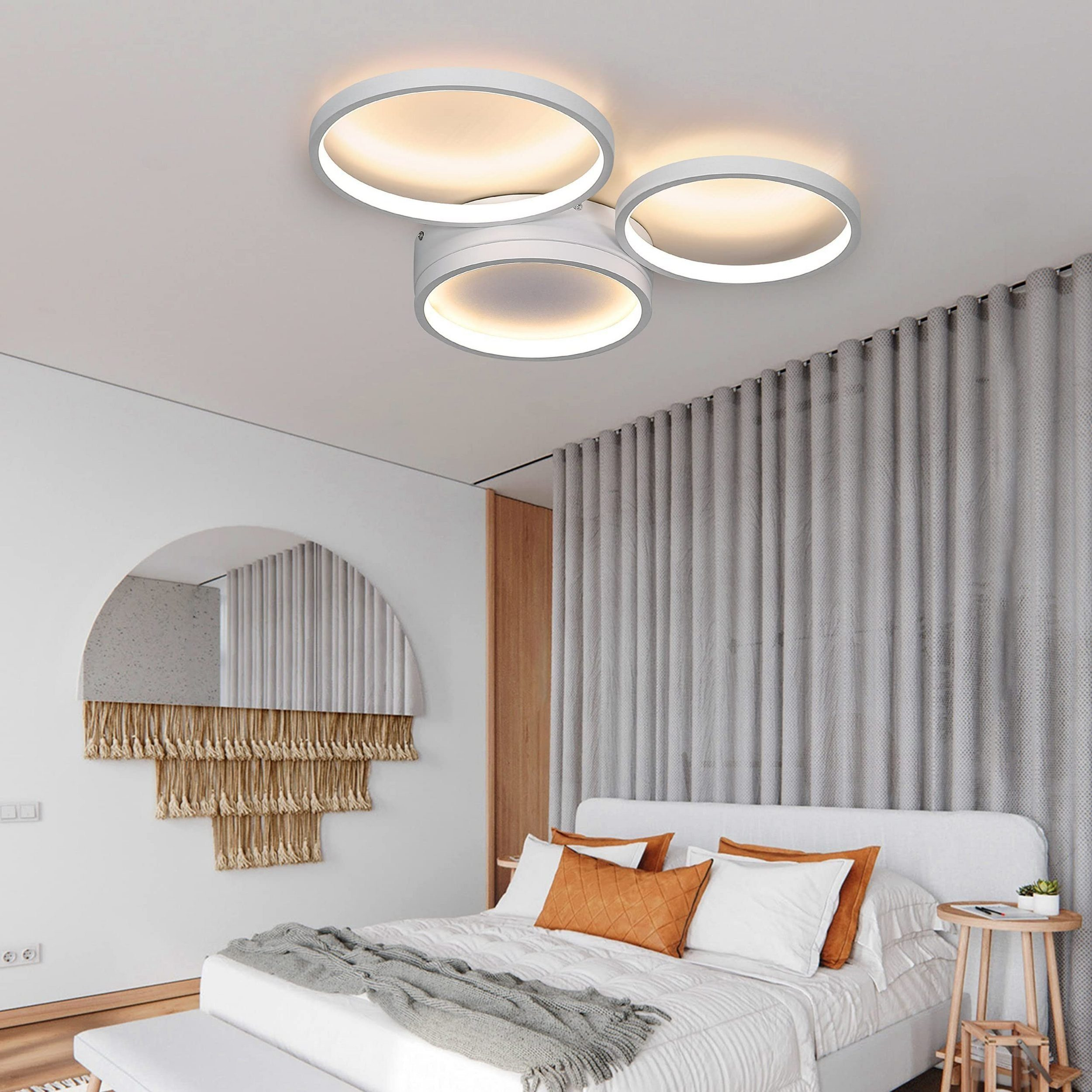 Sypialnia z trzema lampami pierścieniowymi, lustrem i łóżkiem z pomarańczowymi poduszkami.