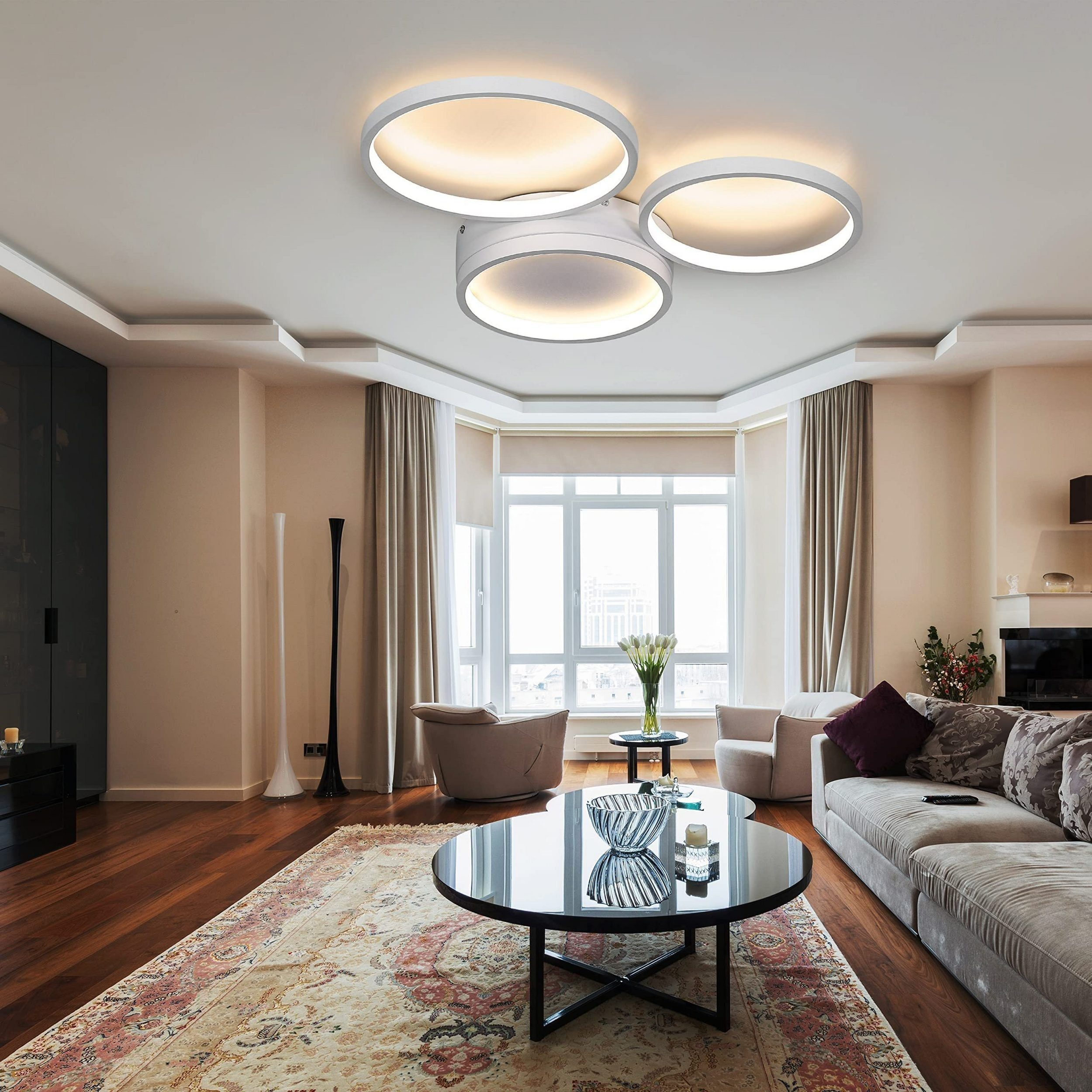 Salon z trzema białymi, okrągłymi lampami sufitowymi, ciemnym stołem i wzorzystym dywanem.