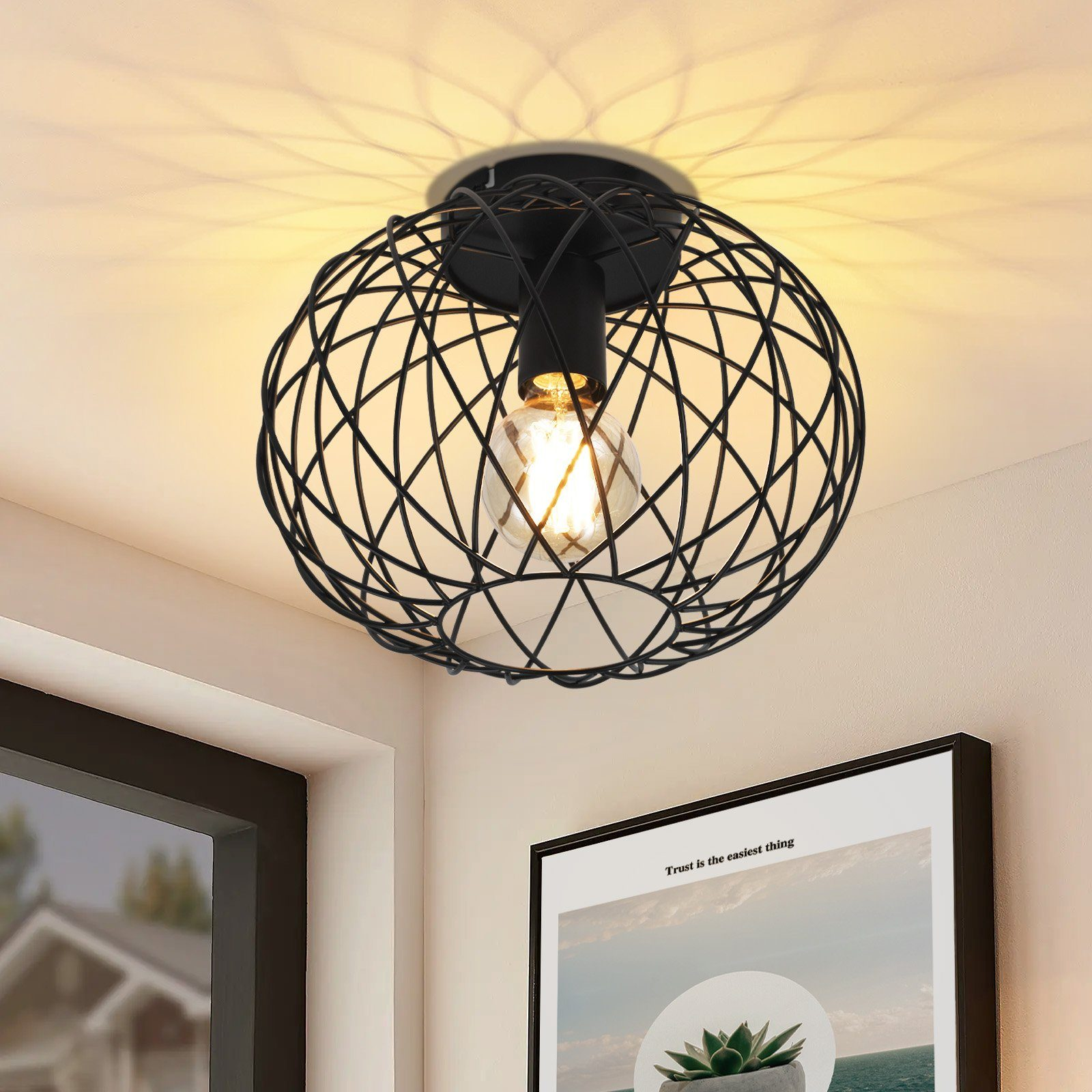 Czarna lampa sufitowa z drucianym stelażem z żarówką. W rogu pokoju ze sztuką i rośliną.