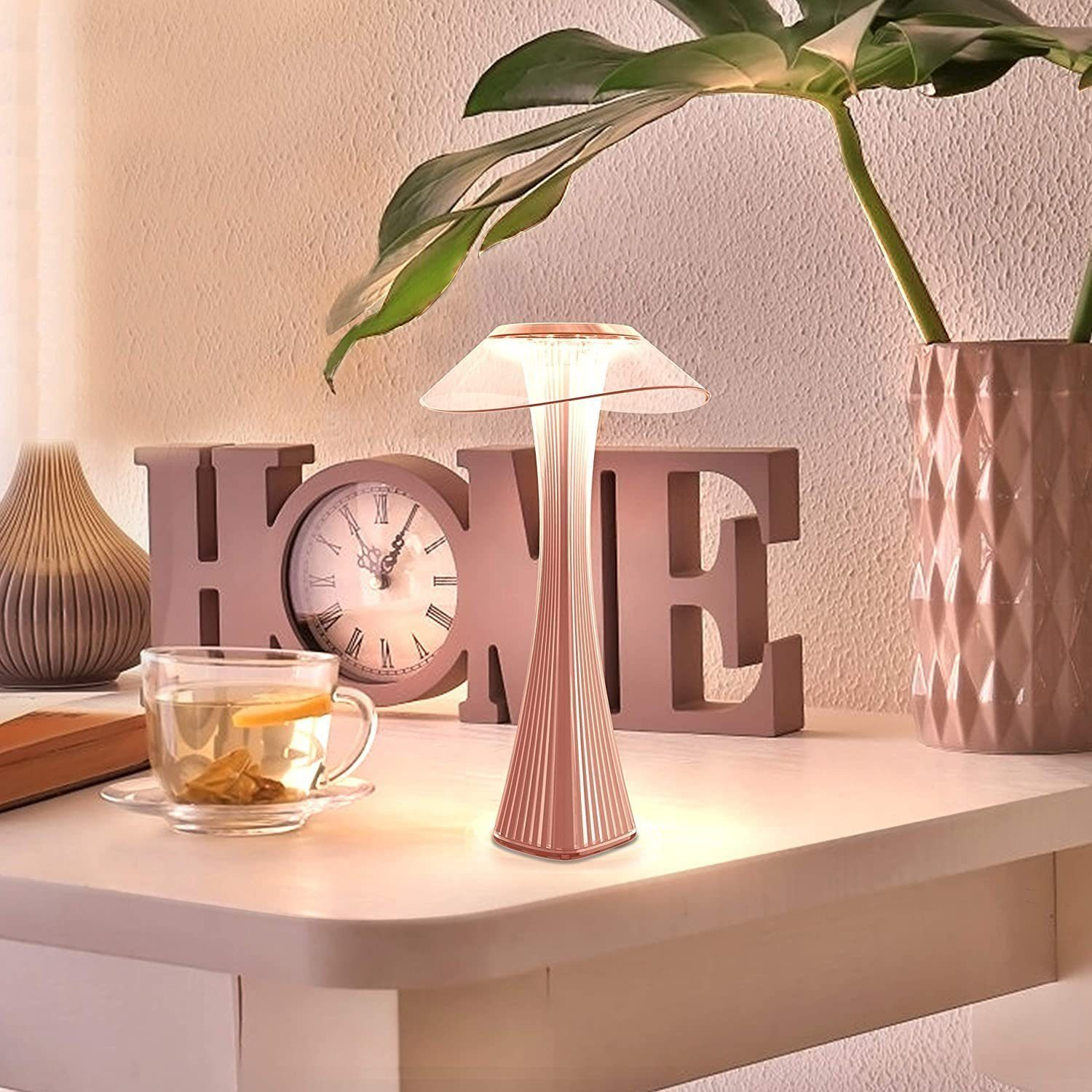 Różowa lampa na stole z filiżanką herbaty, zegarem i dekoracyjnym znakiem HOME.