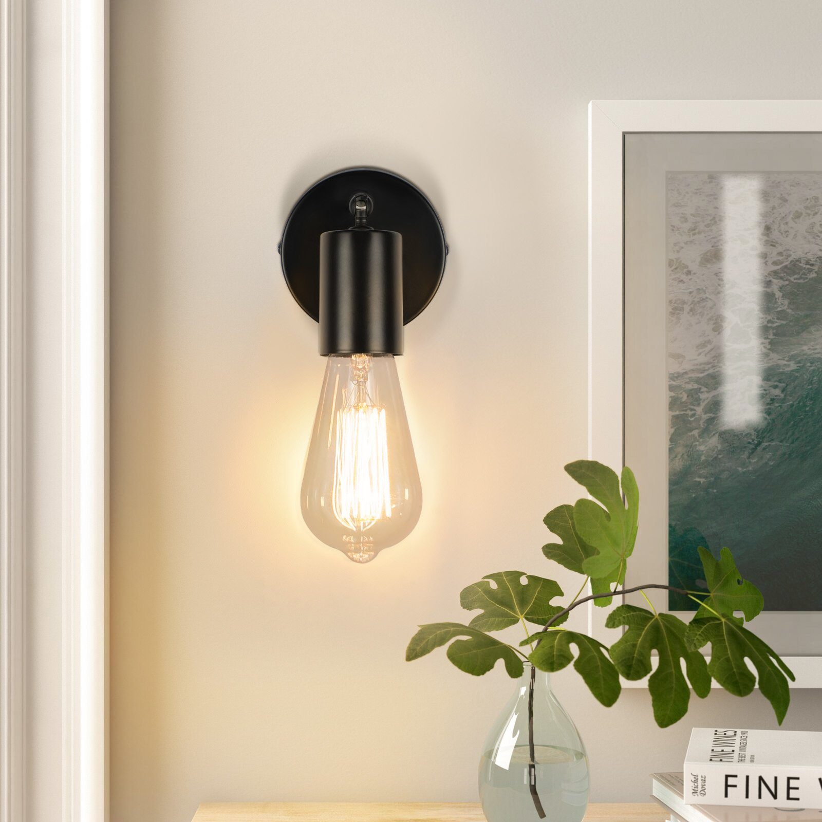 Czarny kinkiet z żarówką na ścianie obok wazonu z liśćmi.