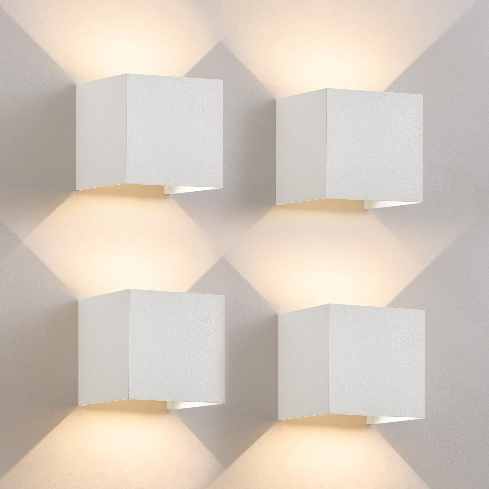 Cztery białe, sześcienne lampy ścienne ze włączonymi światłami, tworzące wzór na ścianie.