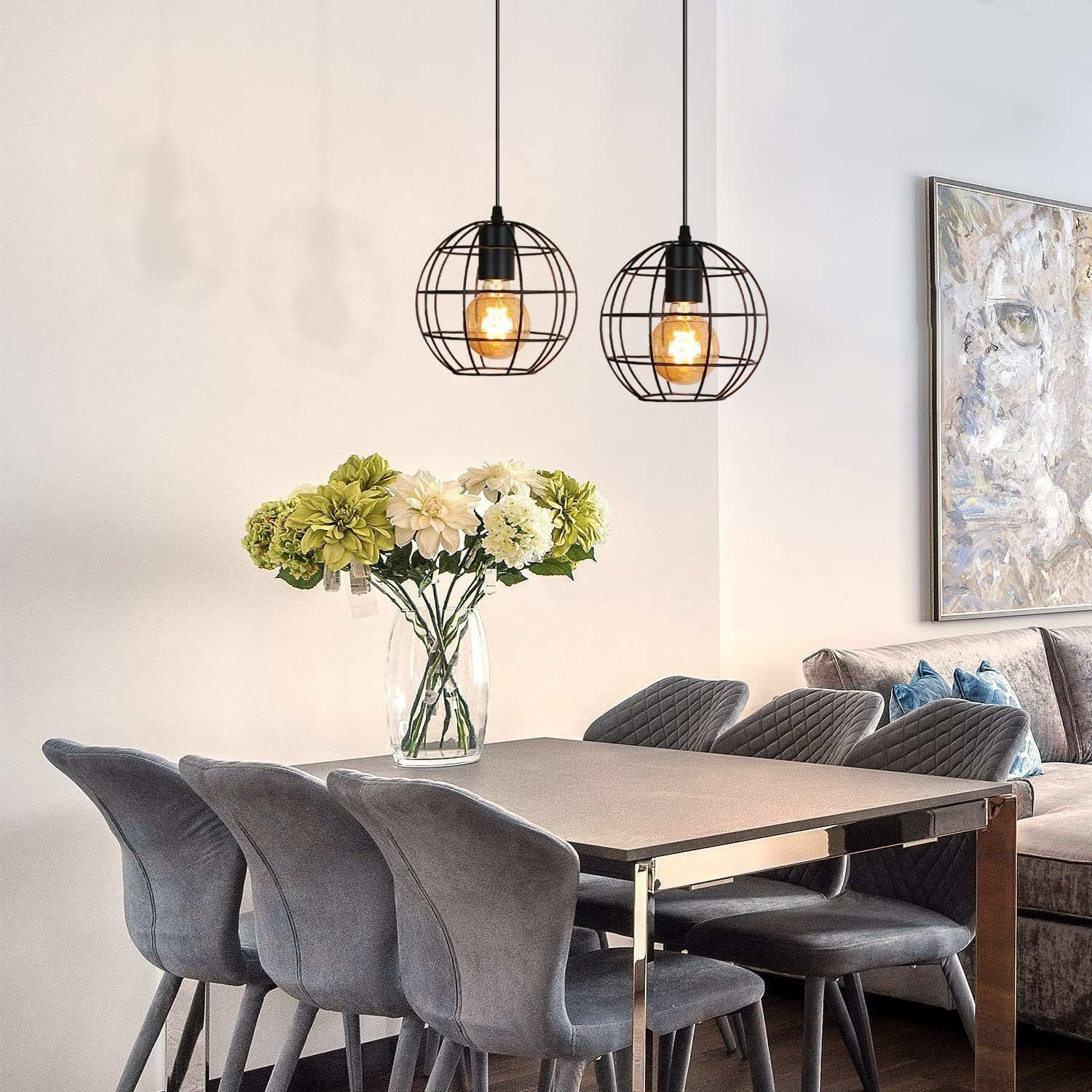 Jadalnia ze stołem, krzesłami i dwoma lampami wiszącymi. Kwiaty w wazonie, dzieło sztuki.