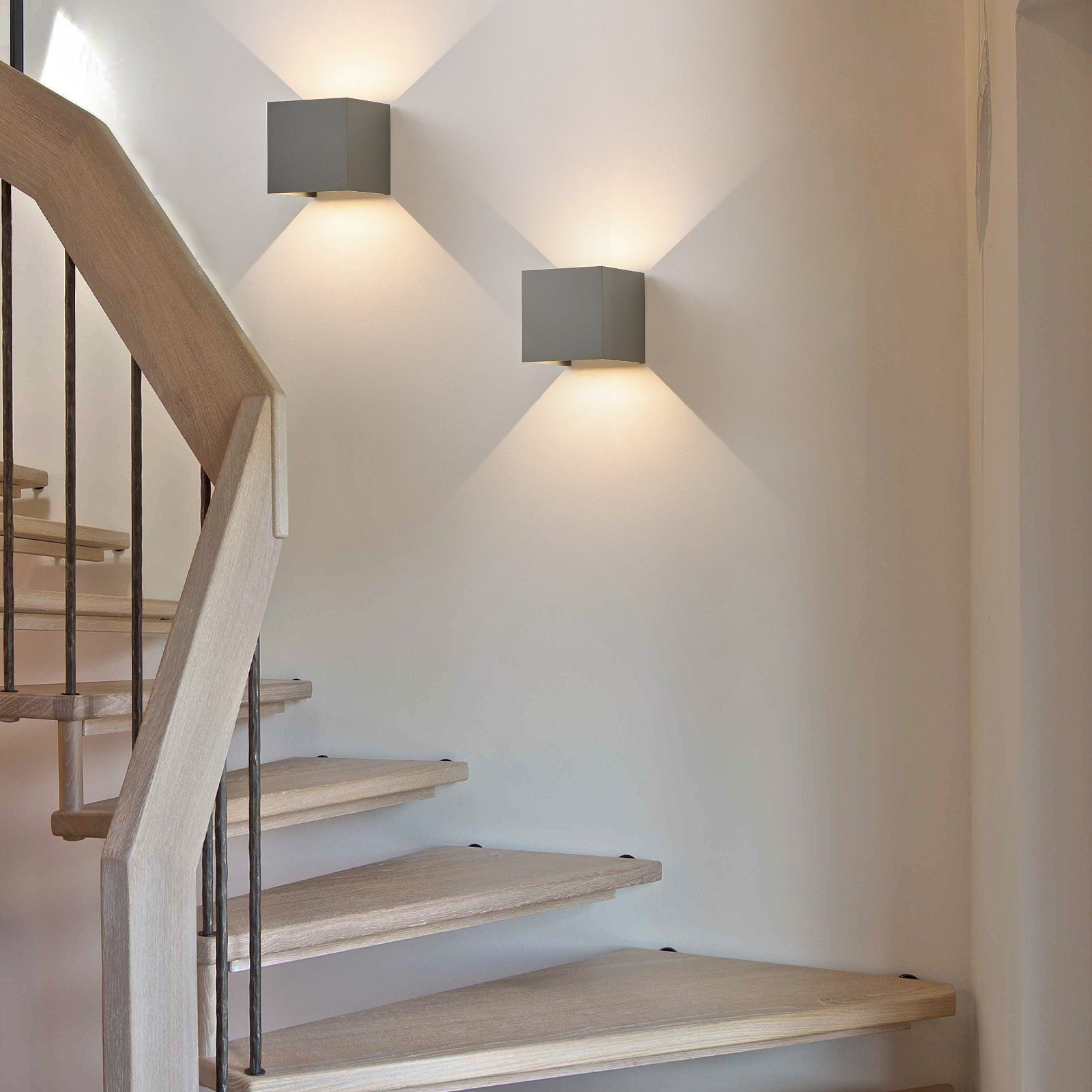 Scala con gradini in legno e ringhiere in metallo scuro, illuminata da applique quadrate.
