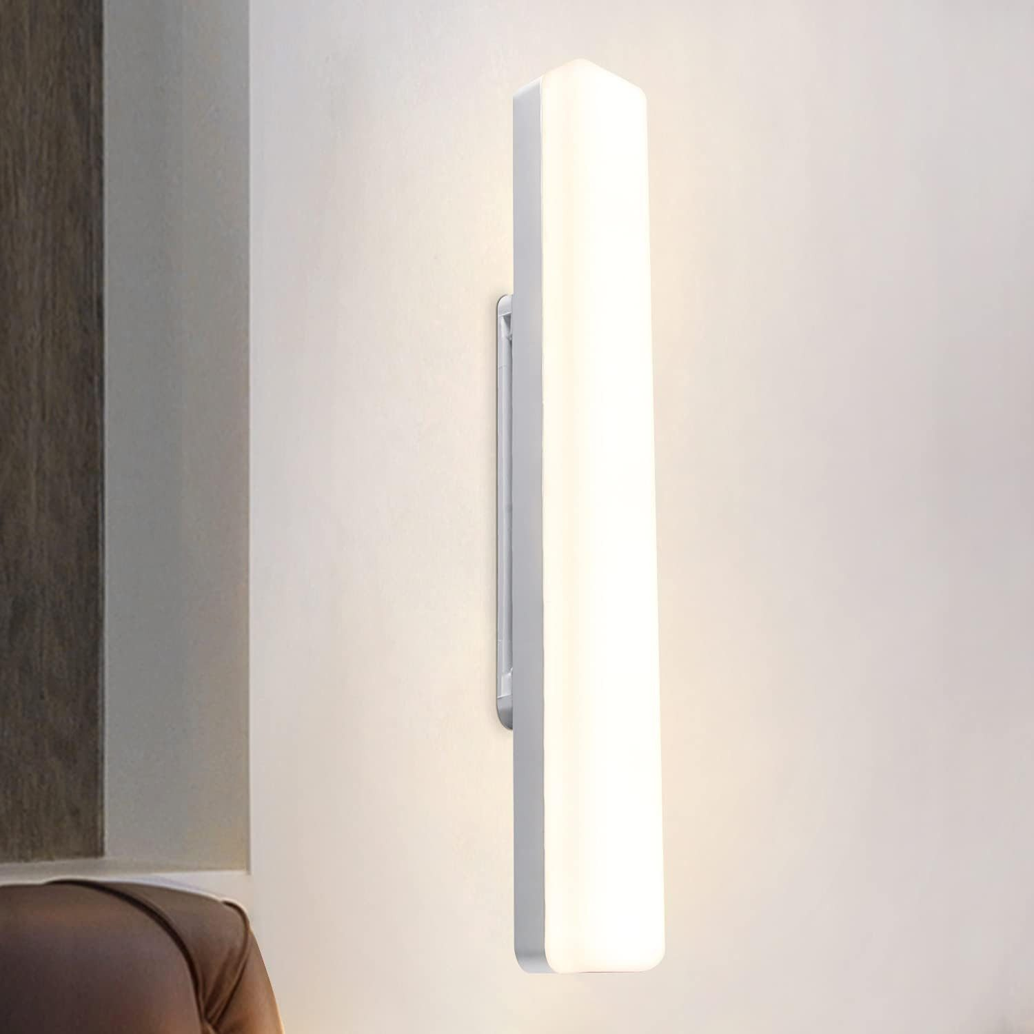 Biała, prostokątna oprawa oświetleniowa montowana na ścianie, oświetlająca ścianę miękkim światłem.