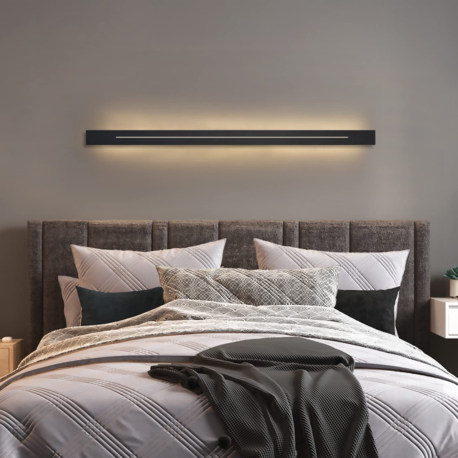 Czarna, liniowa lampa LED nad łóżkiem. Szara ściana i poduszki.