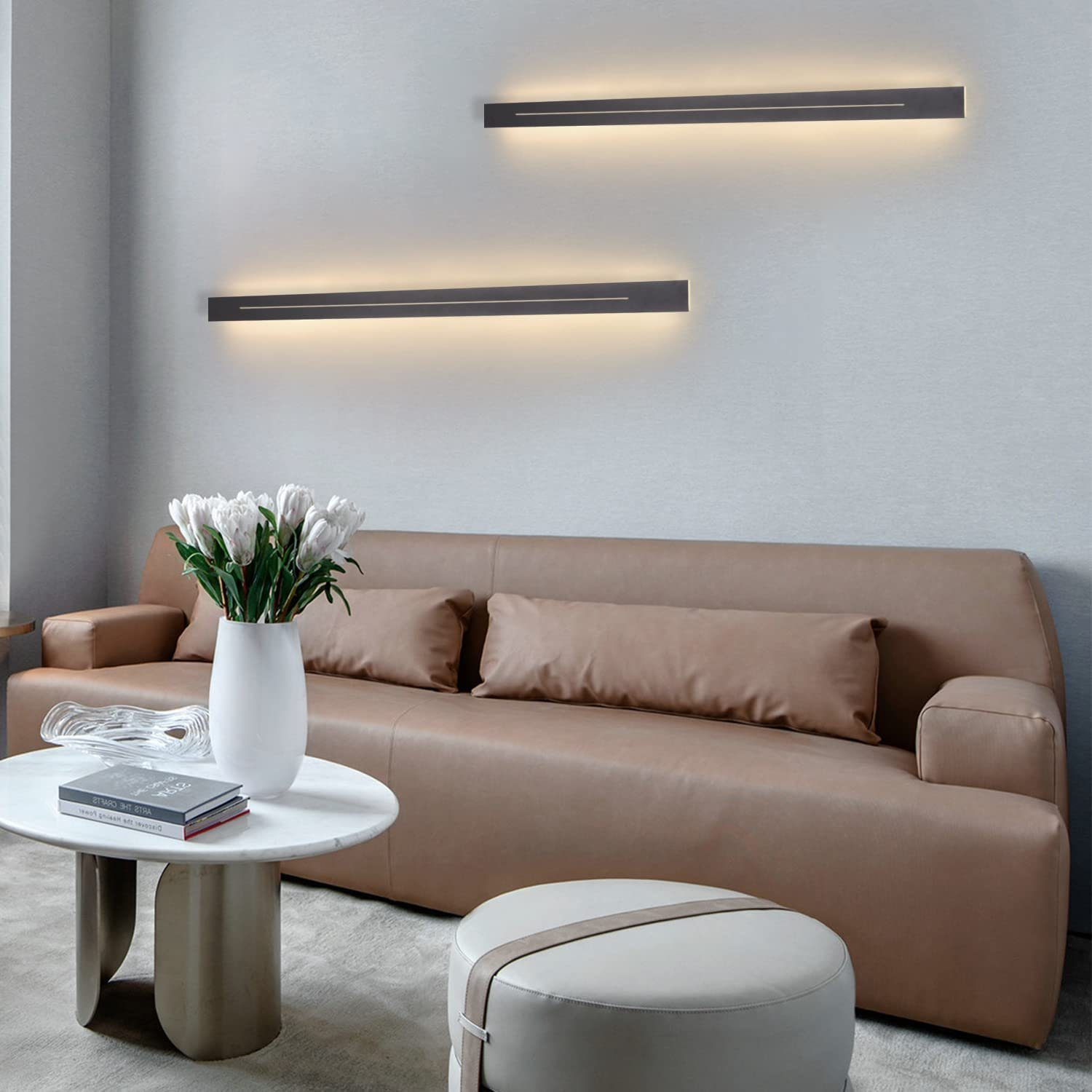 Nowoczesny salon ze skórzaną sofą, stolikiem kawowym i białym wazonem z kwiatami, obok okrągłej pufy.