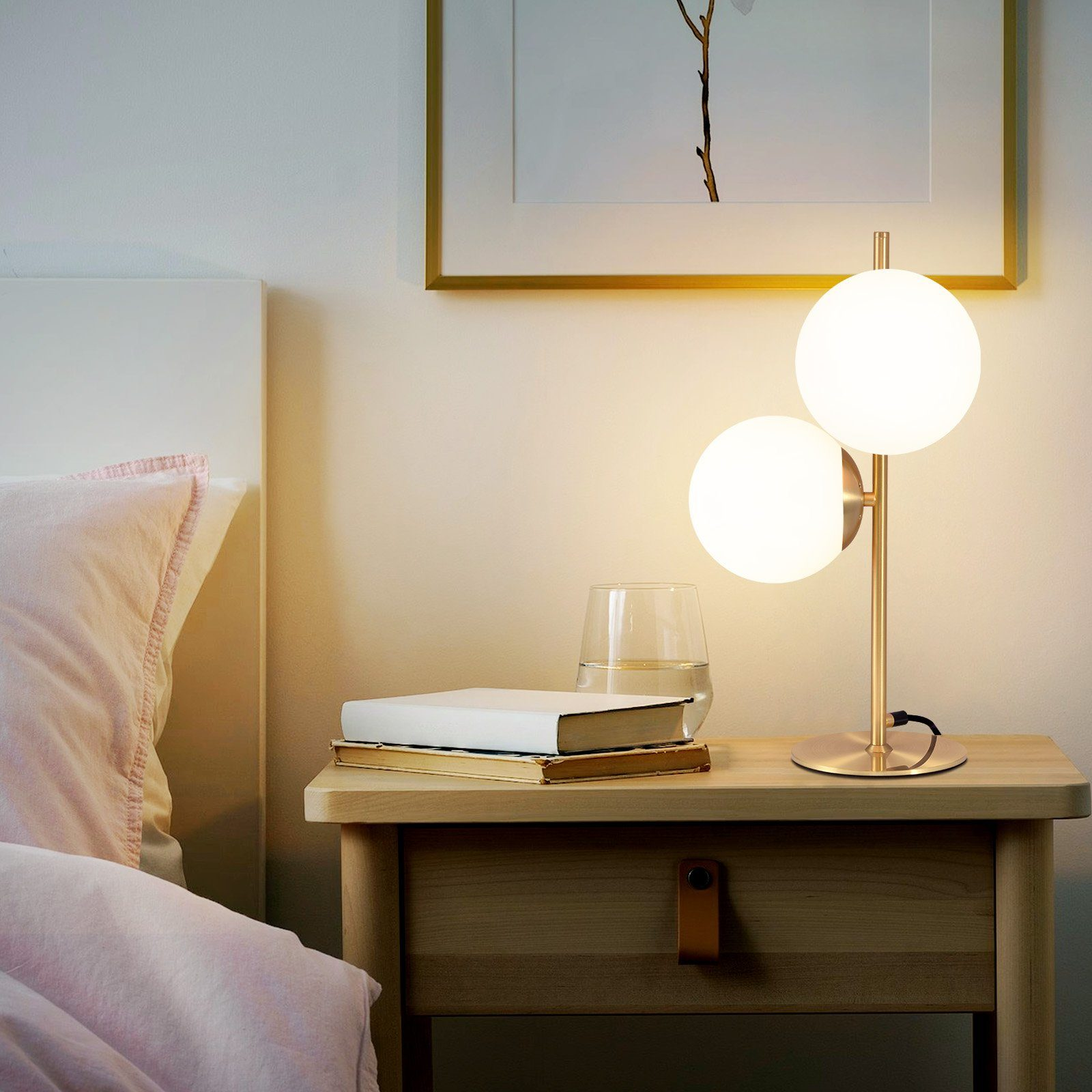 Sypialnia z lampą stołową z dwoma białymi kulami, książkami, szklanką wody i różowym łóżkiem.
