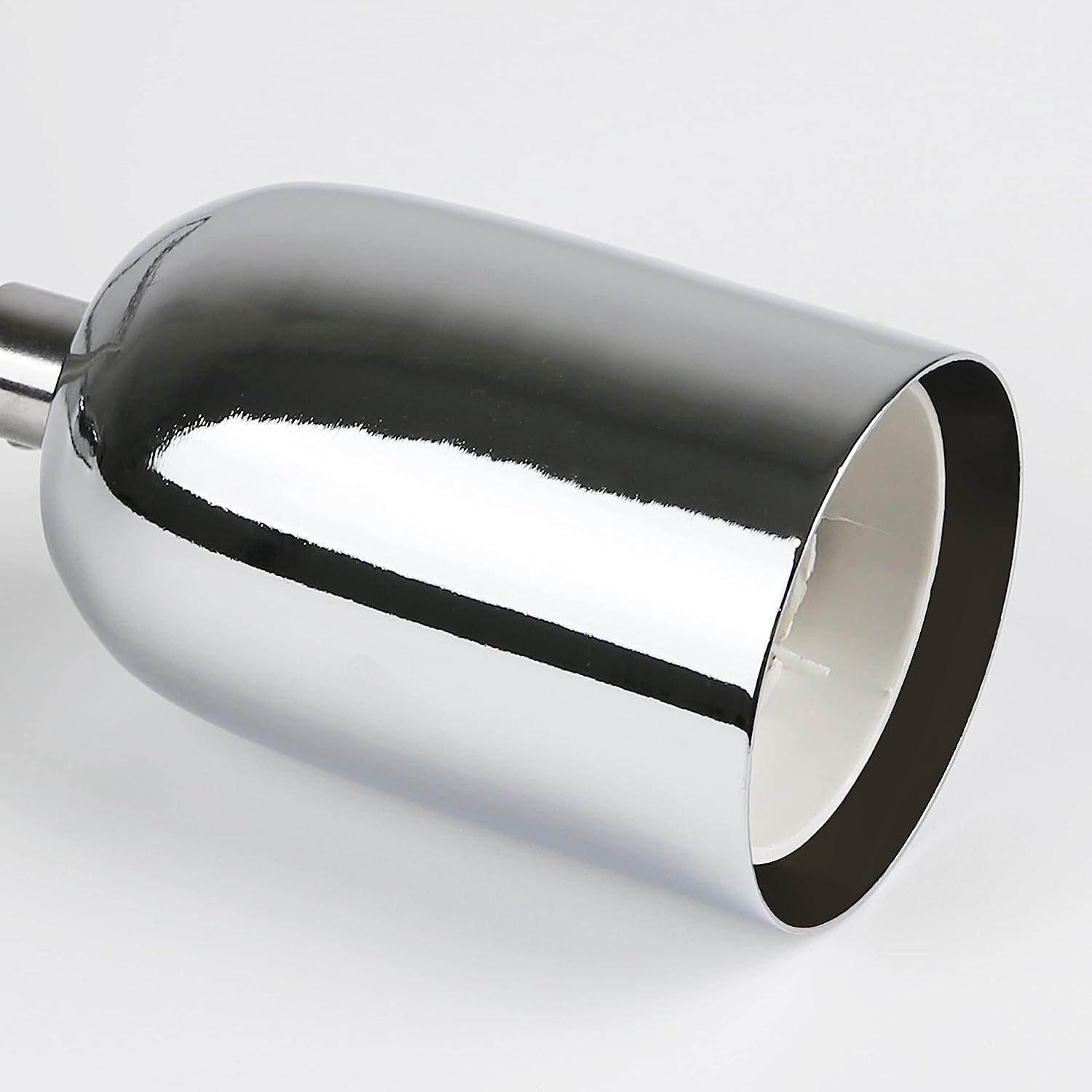 Chromowana głowica lampy z białym wnętrzem, odbijająca światło na białej powierzchni.