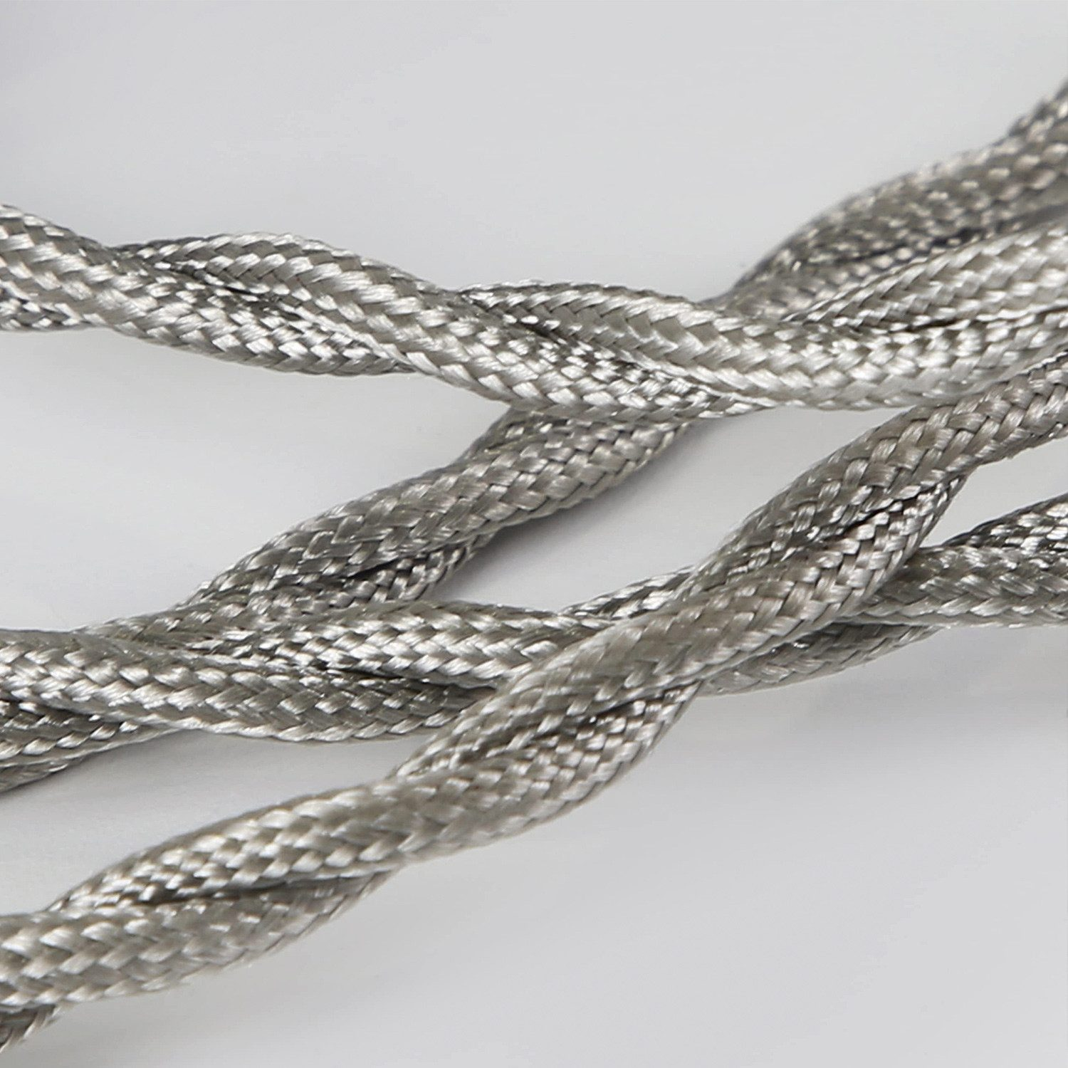 Zbliżenie plecionego srebrnego przewodu elektrycznego, wiele skręconych razem żył. Przewód jest na jasnoszarym tle.