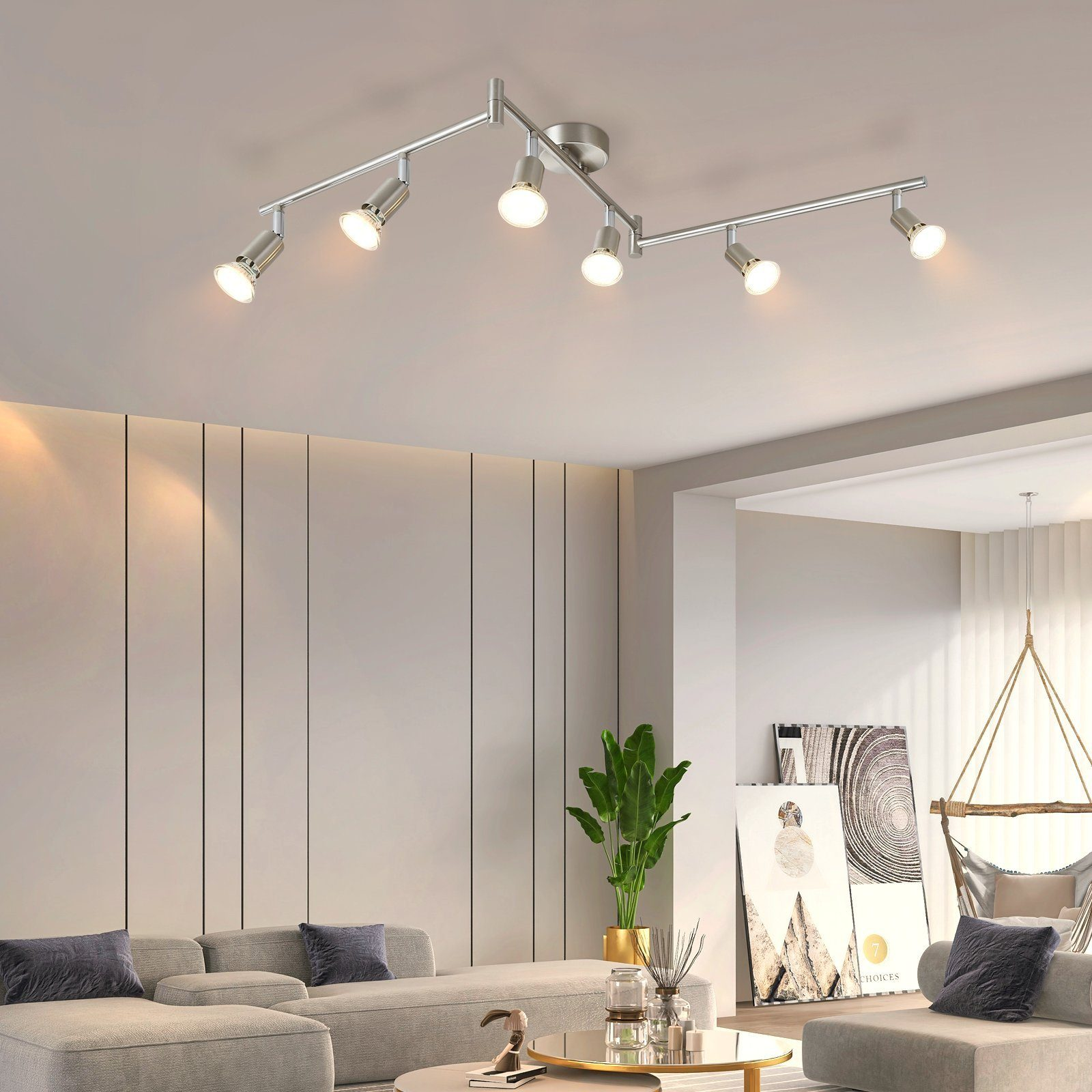 Salon z nowoczesnym systemem oświetlenia szynowego, szarą sofą i dużą rośliną doniczkową.