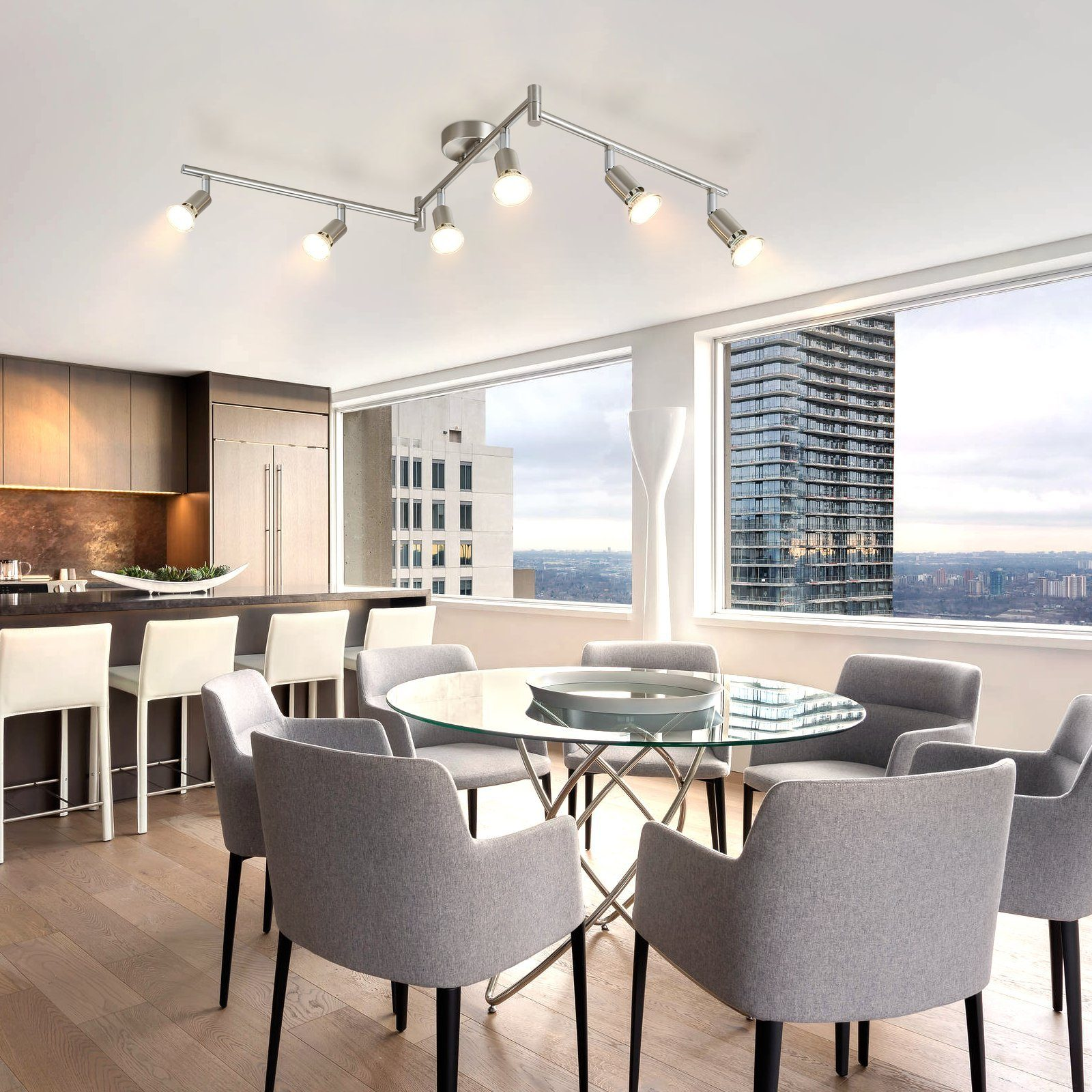 Jadalnia ze szklanym stołem, szarymi krzesłami i lampą sufitową. Widok na miasto za oknami.