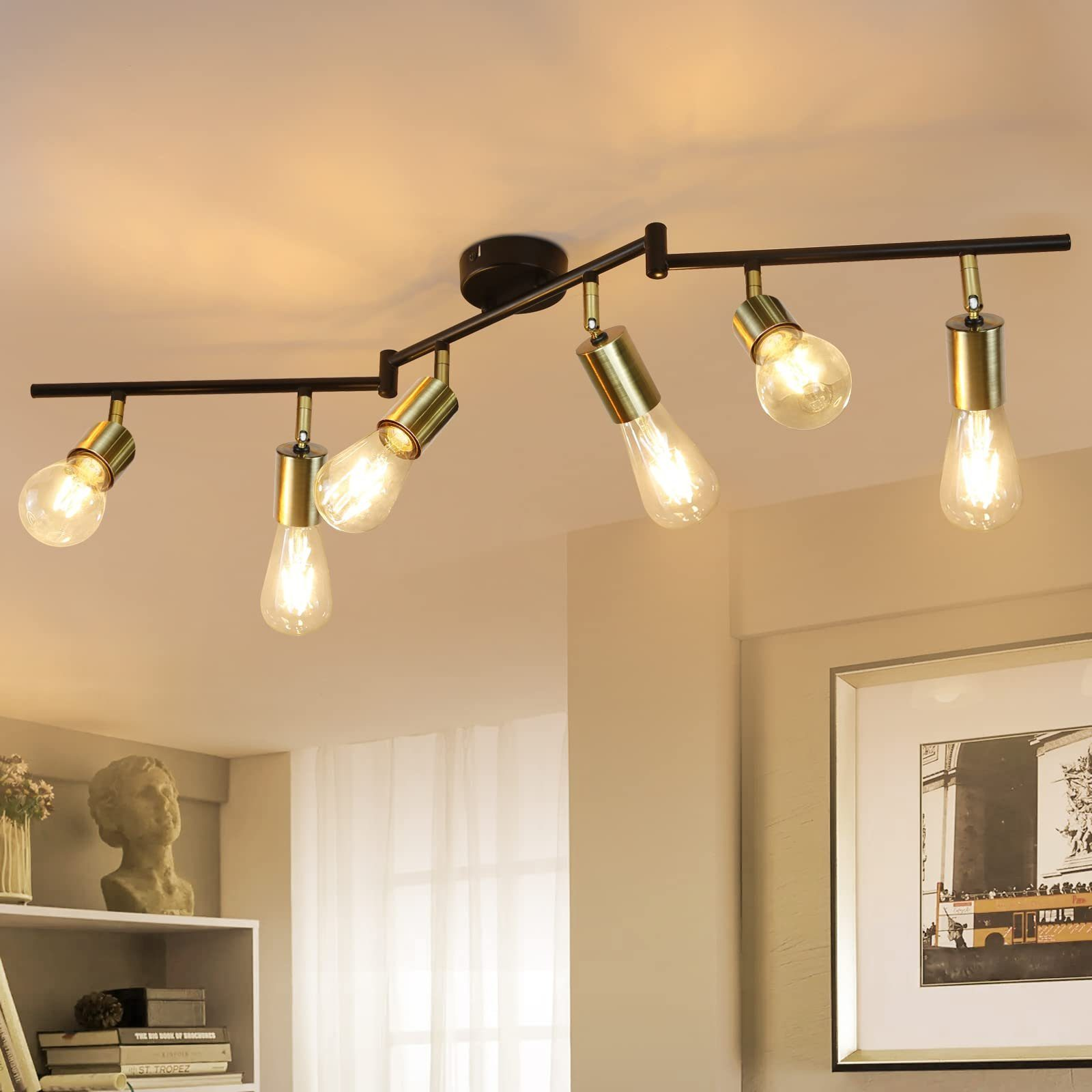 Lampa sufitowa z sześcioma światłami na czarnym drążku. Tło obejmuje popiersie i obraz.