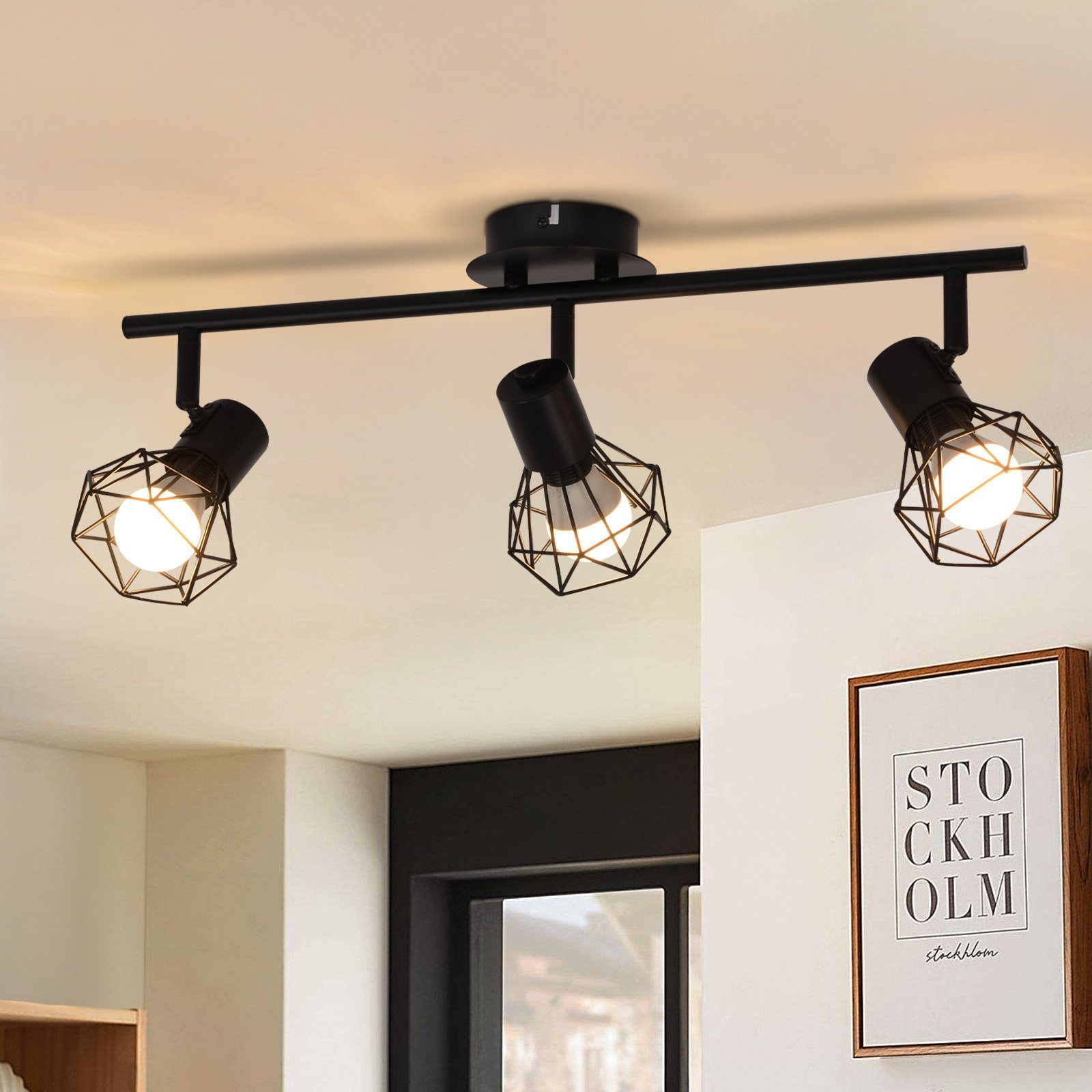 Soffitto con tre faretti neri, ciascuno con un design a gabbia. È visibile un'immagine incorniciata.