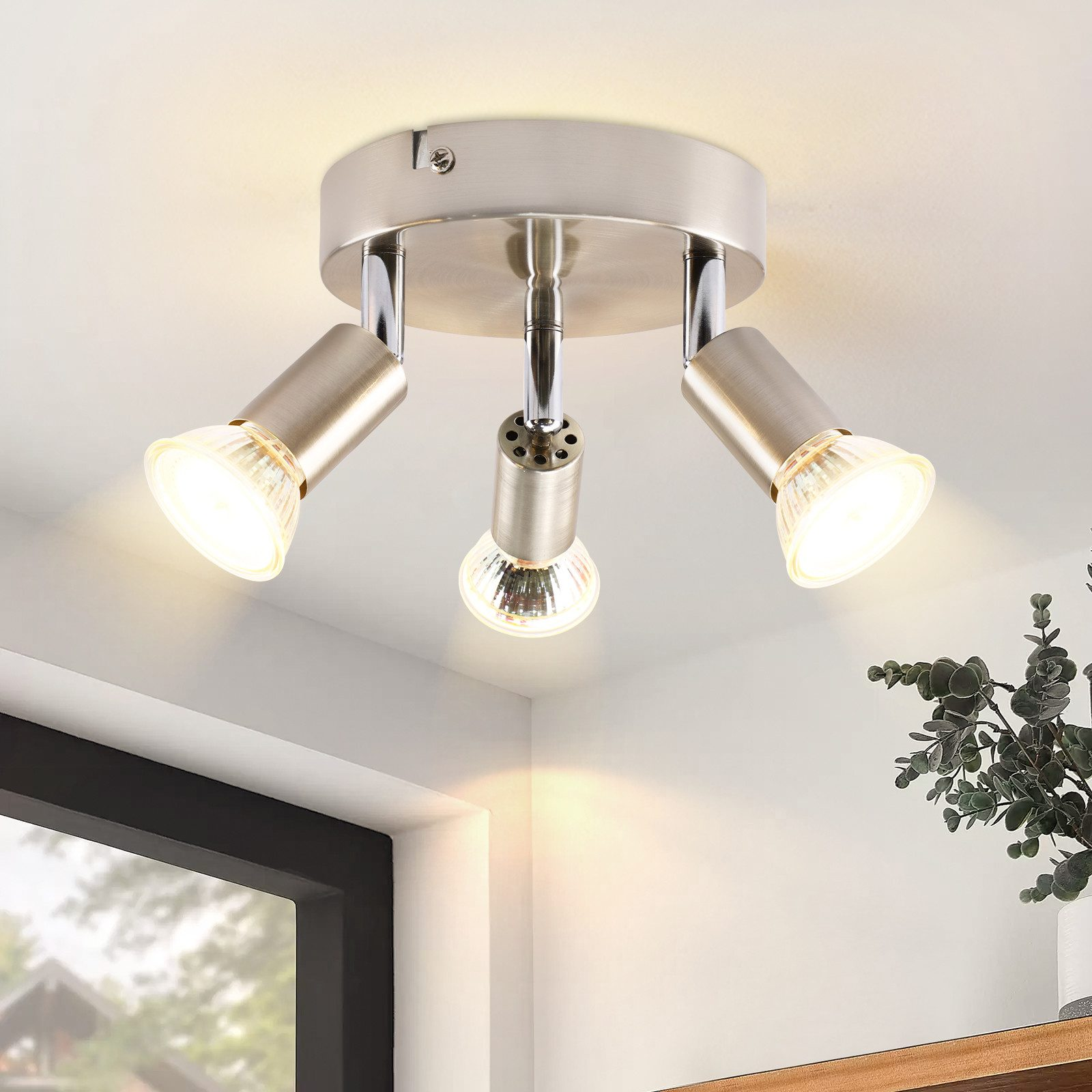 Faretto argentato montato a soffitto. Tre luci sono visibili. Sfondo bianco.