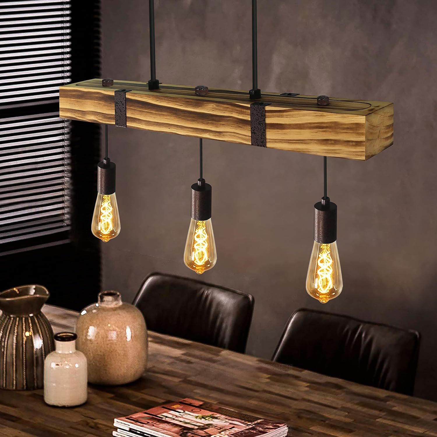 Lampada a sospensione con trave in legno e tre lampadine Edison su un tavolo di legno con decorazioni.